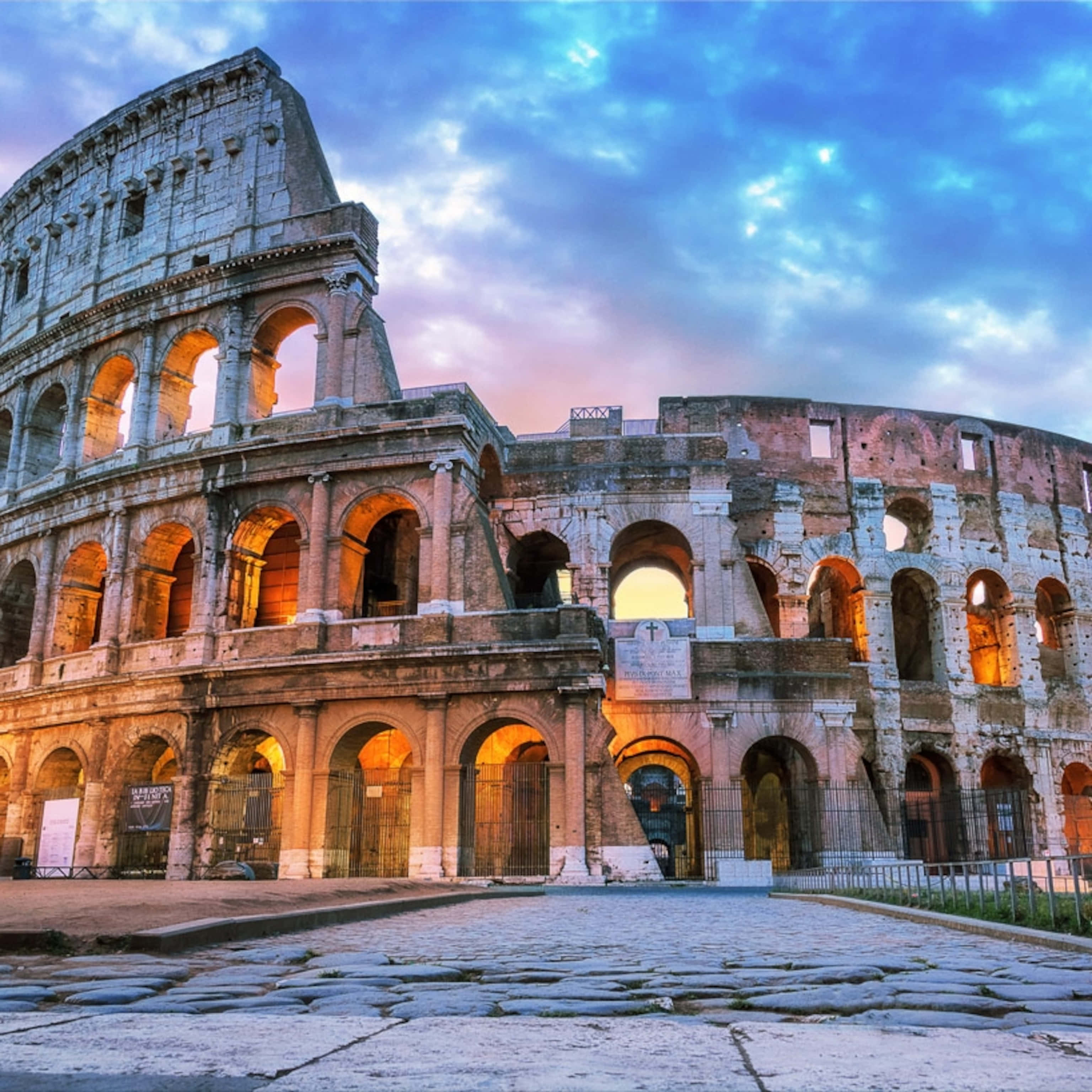 Roman 桌布 壁紙 — 古老的羅馬競技場在暮色天空下巍然聳立，溫暖的室內燈光透過拱門閃爍。