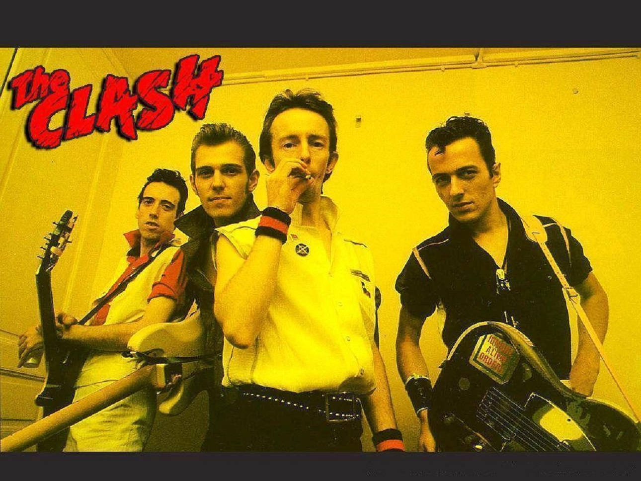 English 桌布 壁紙 — The Clash 樂團成員在黃色牆壁前擺出強烈姿勢，牆上有紅色塗鴉風格的樂團名稱。