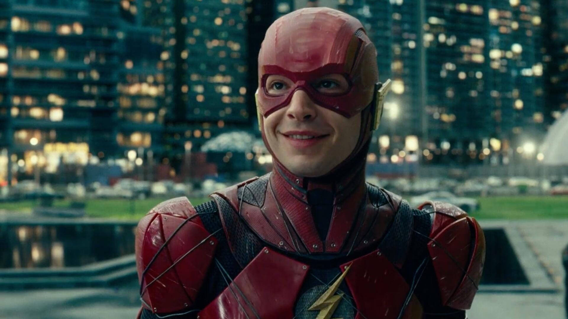 閃電俠 桌布 壁紙 — The Flash 身穿紅色戰衣，在夜晚模糊的城市天際線前自信微笑。