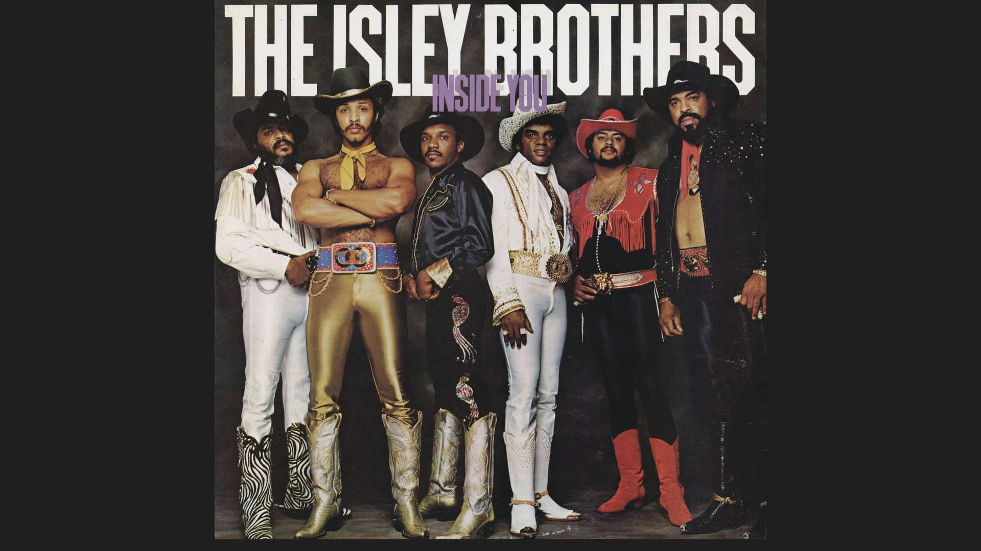 音樂 桌布 壁紙 — The Isley Brothers 在深色背景前自信地擺姿勢，穿著閃亮的70年代牛仔風格服裝，飾有亮片和寬邊帽。