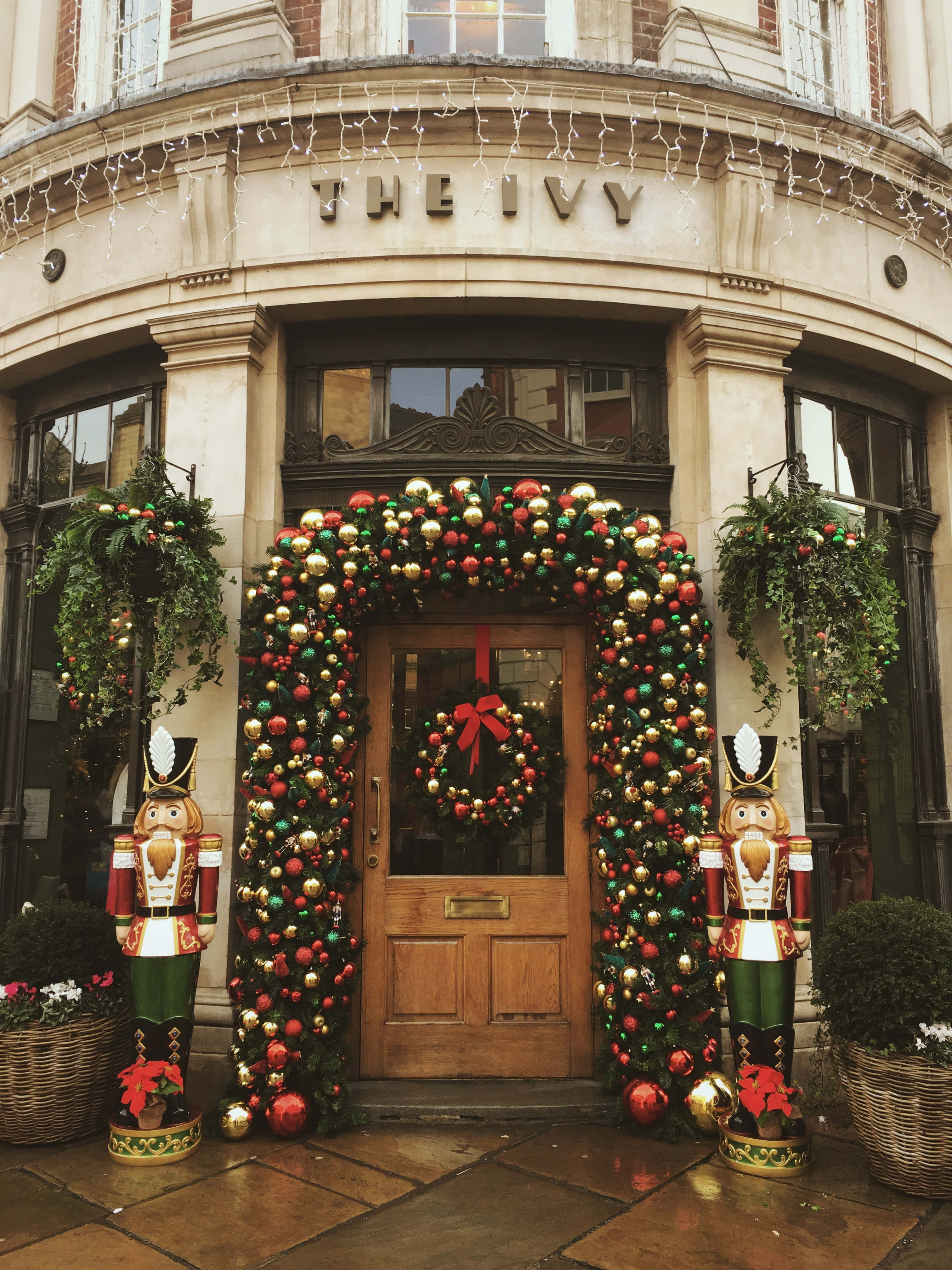 York 桌布 壁紙 — The Ivy 餐廳的節日聖誕入口，裝飾著紅色、金色和綠色的飾品、胡桃夾子雕像和閃爍的燈光。