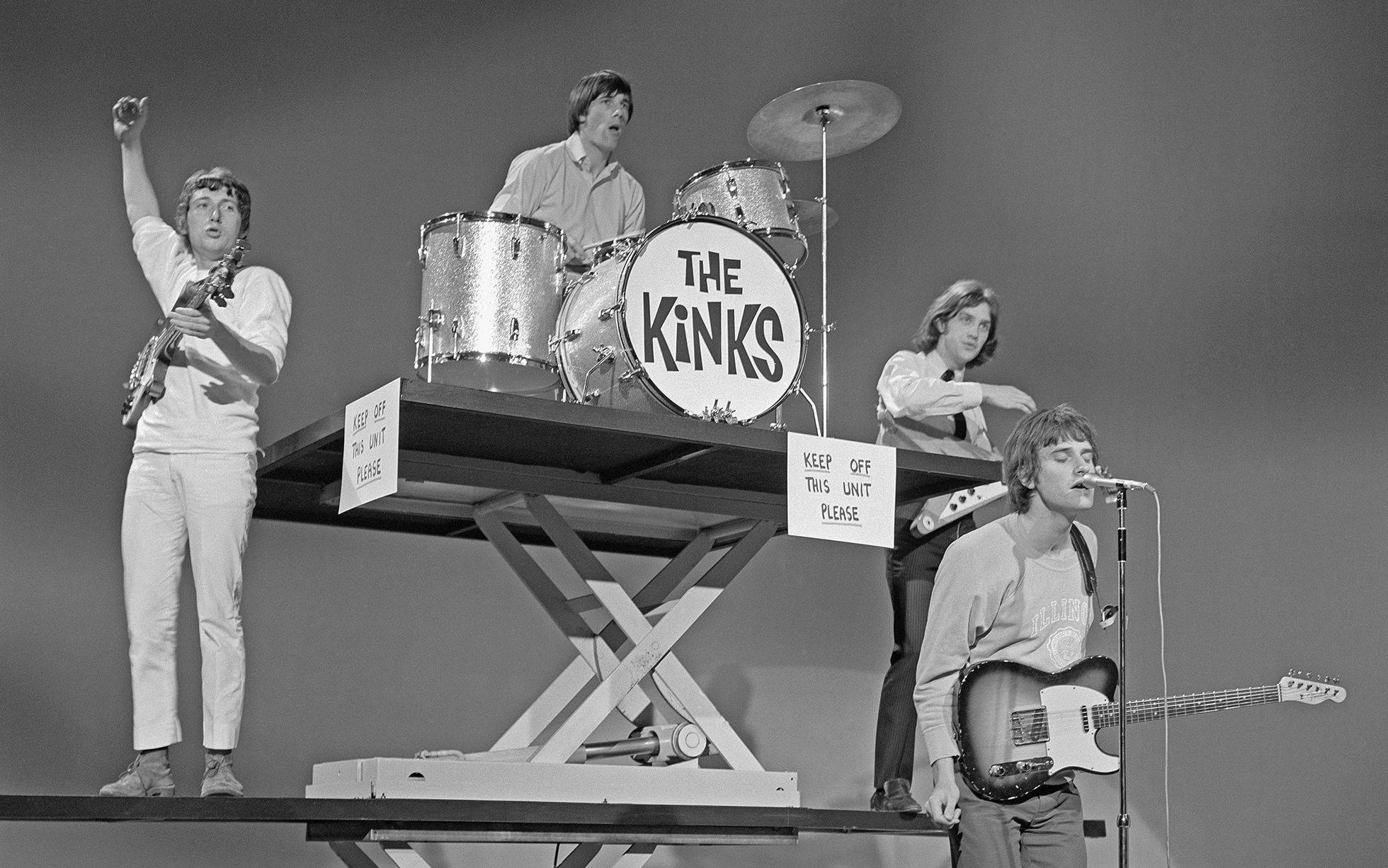 Retro 桌布 壁紙 — The Kinks 在一個升高平台上表演，配有鼓組和吉他，黑白照片。