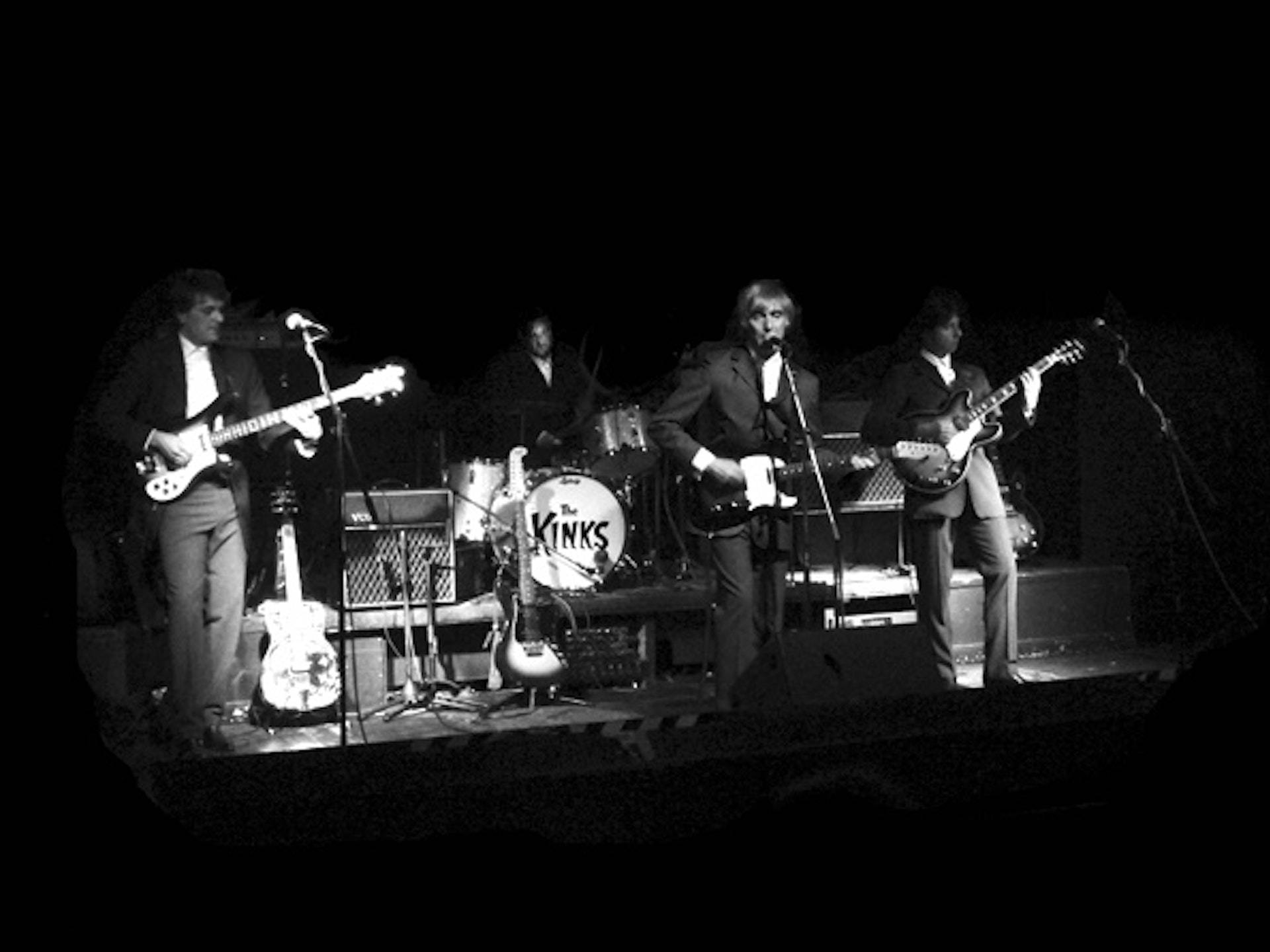 Retro 桌布 壁紙 — The Kinks 在昏暗聚光燈下現場表演吉他和鼓的黑白照片。