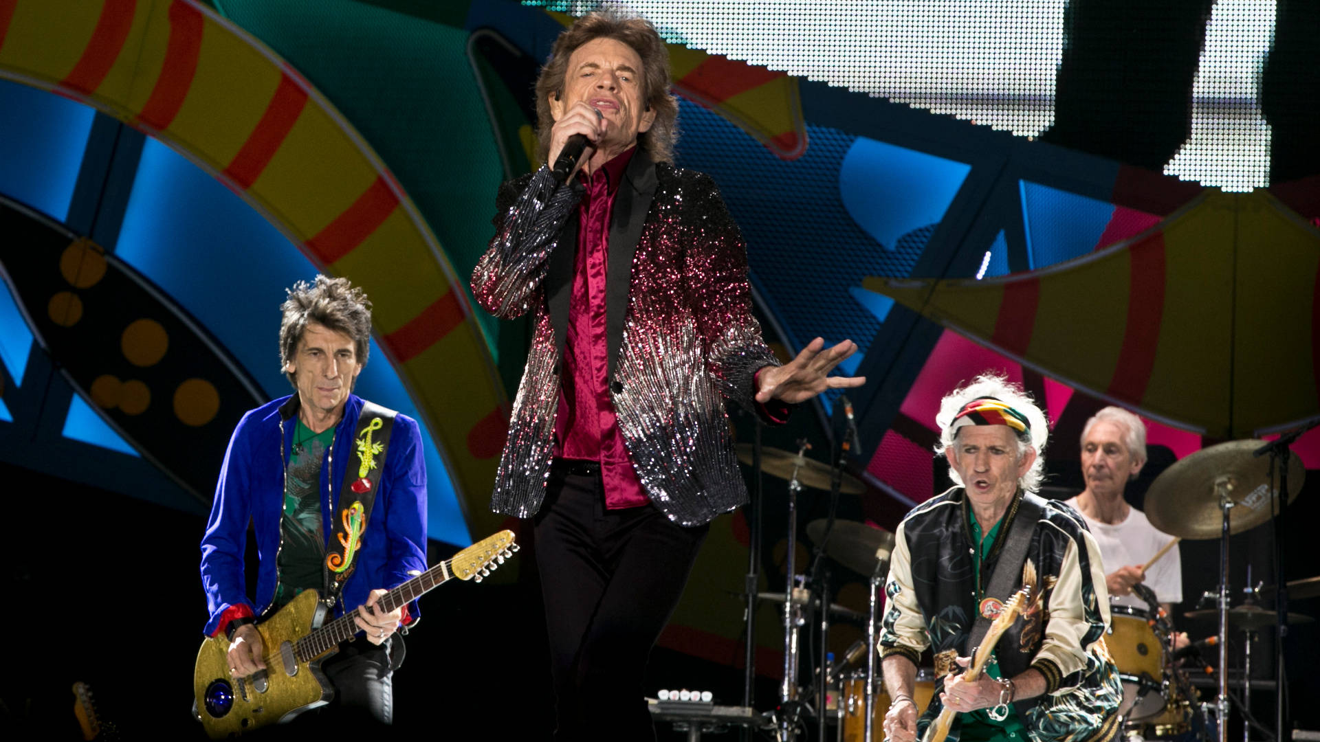 Rock 桌布 壁紙 — The Rolling Stones 在舞台上充滿活力地演出，伴隨著鮮豔多彩的燈光和閃閃發光的夾克。