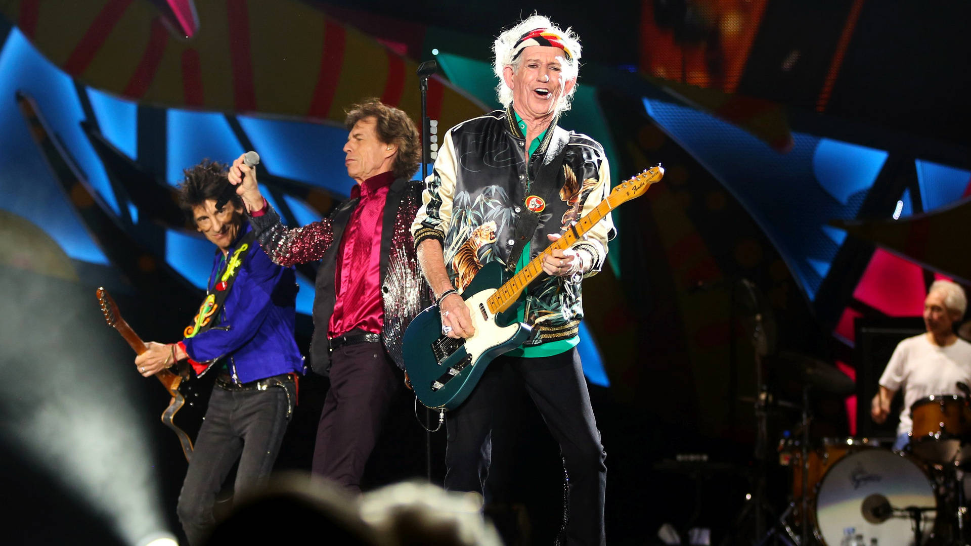 岩石 桌布 壁紙 — The Rolling Stones 在明亮的舞台燈光下，以充滿活力的燈光和色彩繽紛的服裝在舞台上充滿活力地表演。