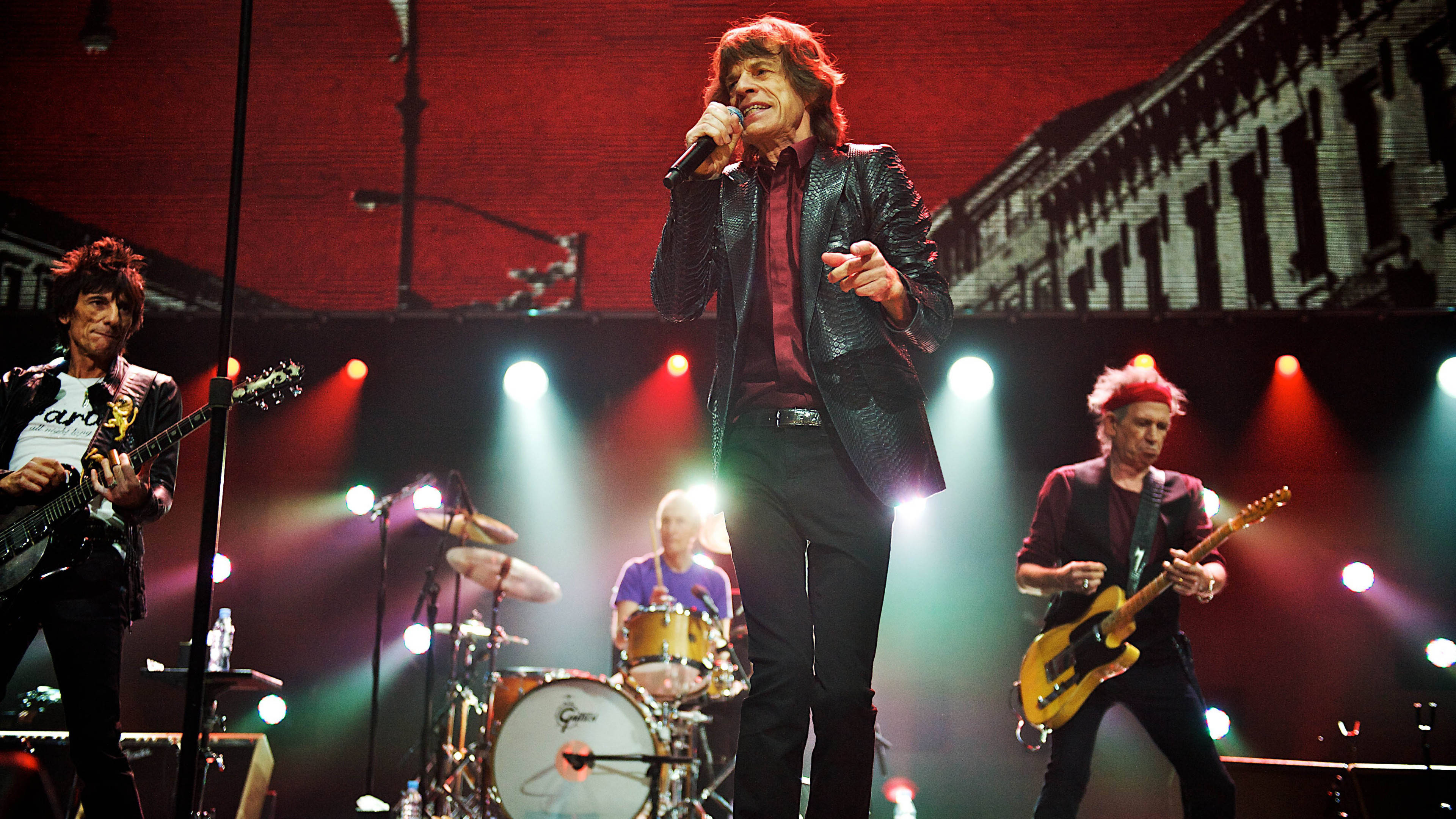 Rock 桌布 壁紙 — The Rolling Stones 在鮮紅和白色聚光燈下，以磚牆為背景，充滿活力地在舞台上表演。