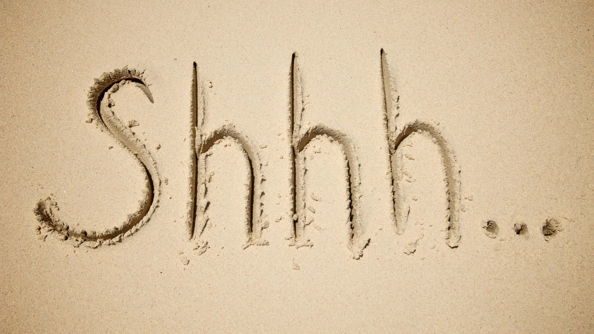  壁紙 — 「Shhh...」這個字用有紋理的筆畫寫在沙子上，在米色的沙灘表面傳達寧靜。
