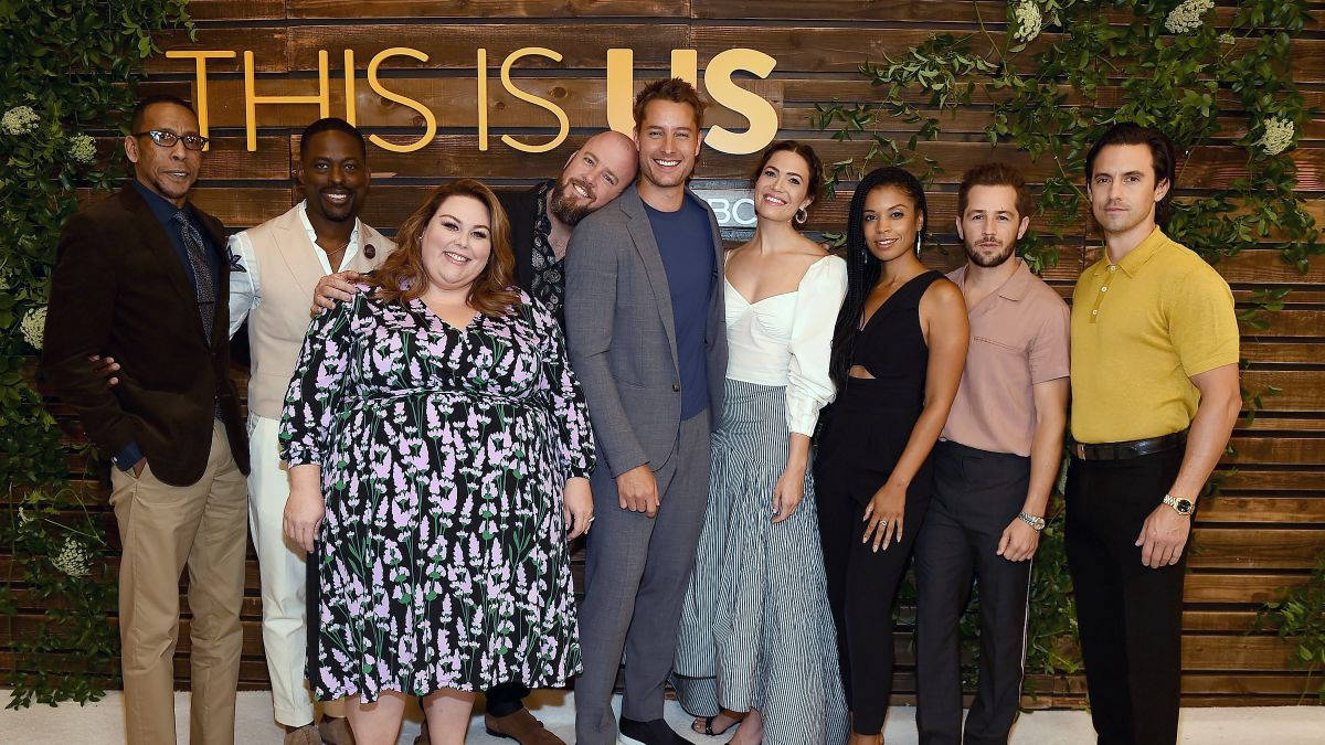 Entertainment 桌布 壁紙 — 《This Is Us》的演員在有綠色植物和節目名稱標牌的木牆前面微笑擺姿勢。