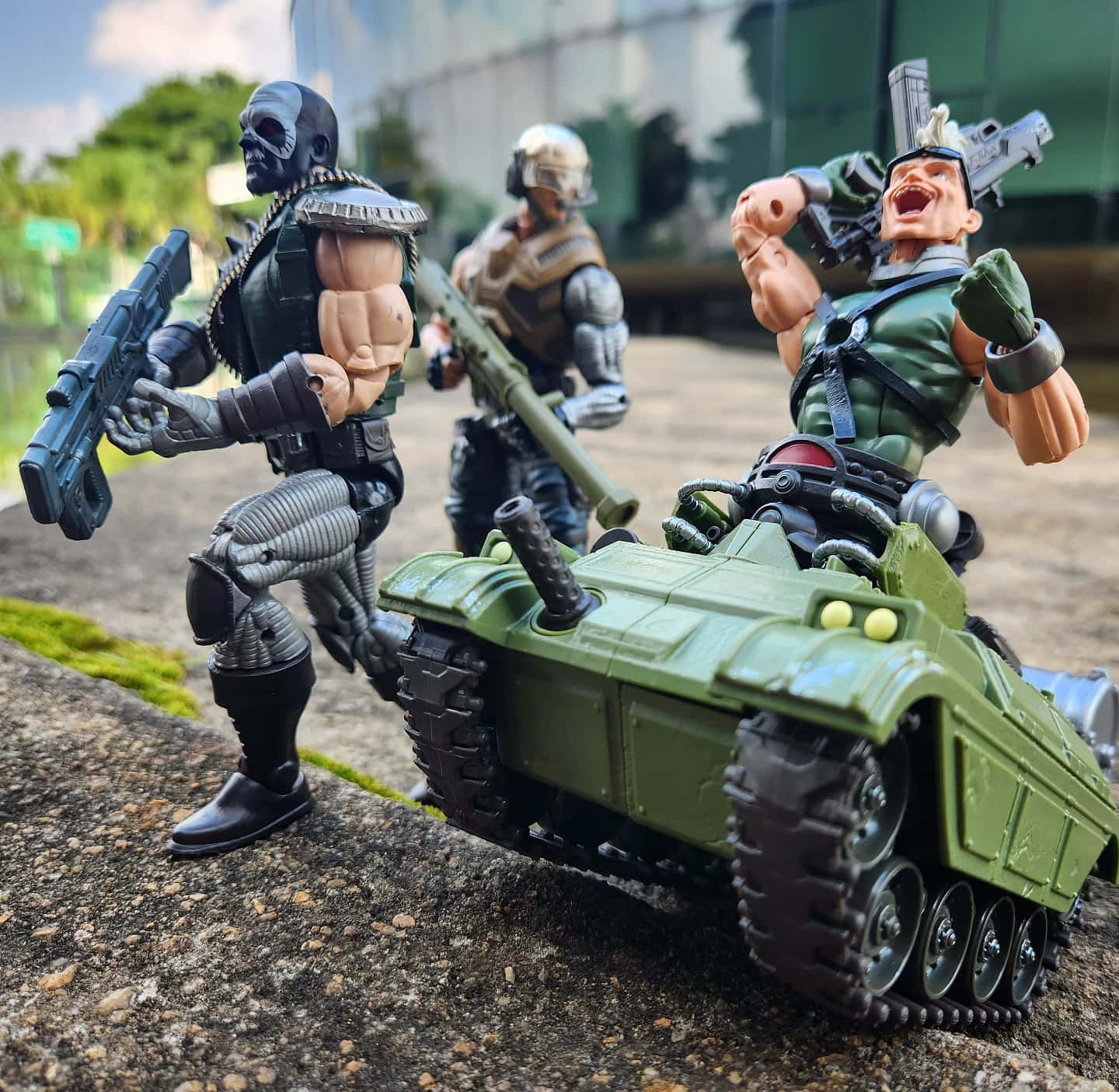 壁紙 — 三個穿著軍裝的動作人偶在戶外岩石表面上與一輛綠色坦克戲劇性地擺姿勢。