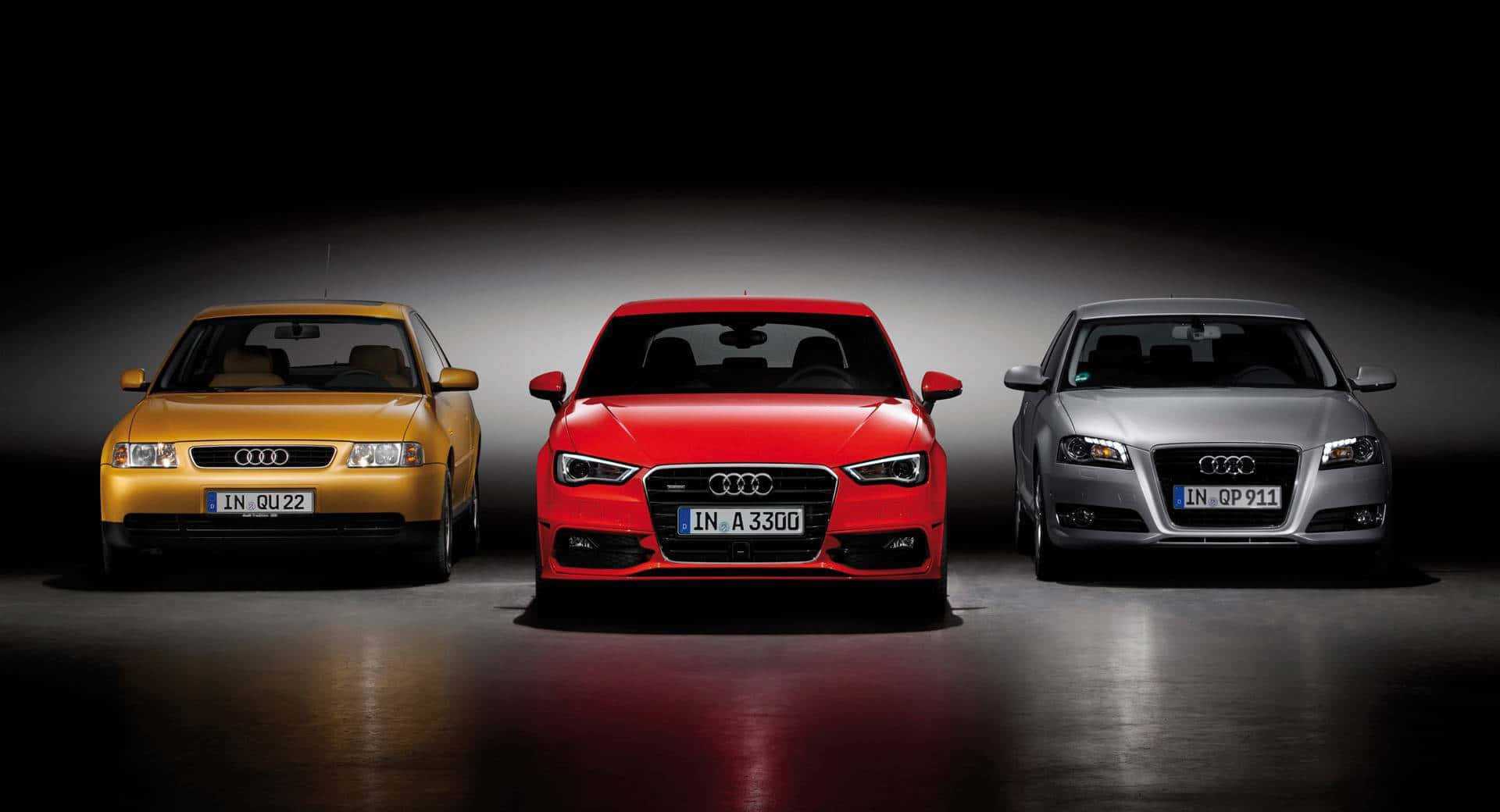 Audi A3 桌布 壁紙 — 三輛黃色、紅色和銀色的奧迪轎車在反射性地板上正面朝前，處於戲劇性的工作室燈光下。