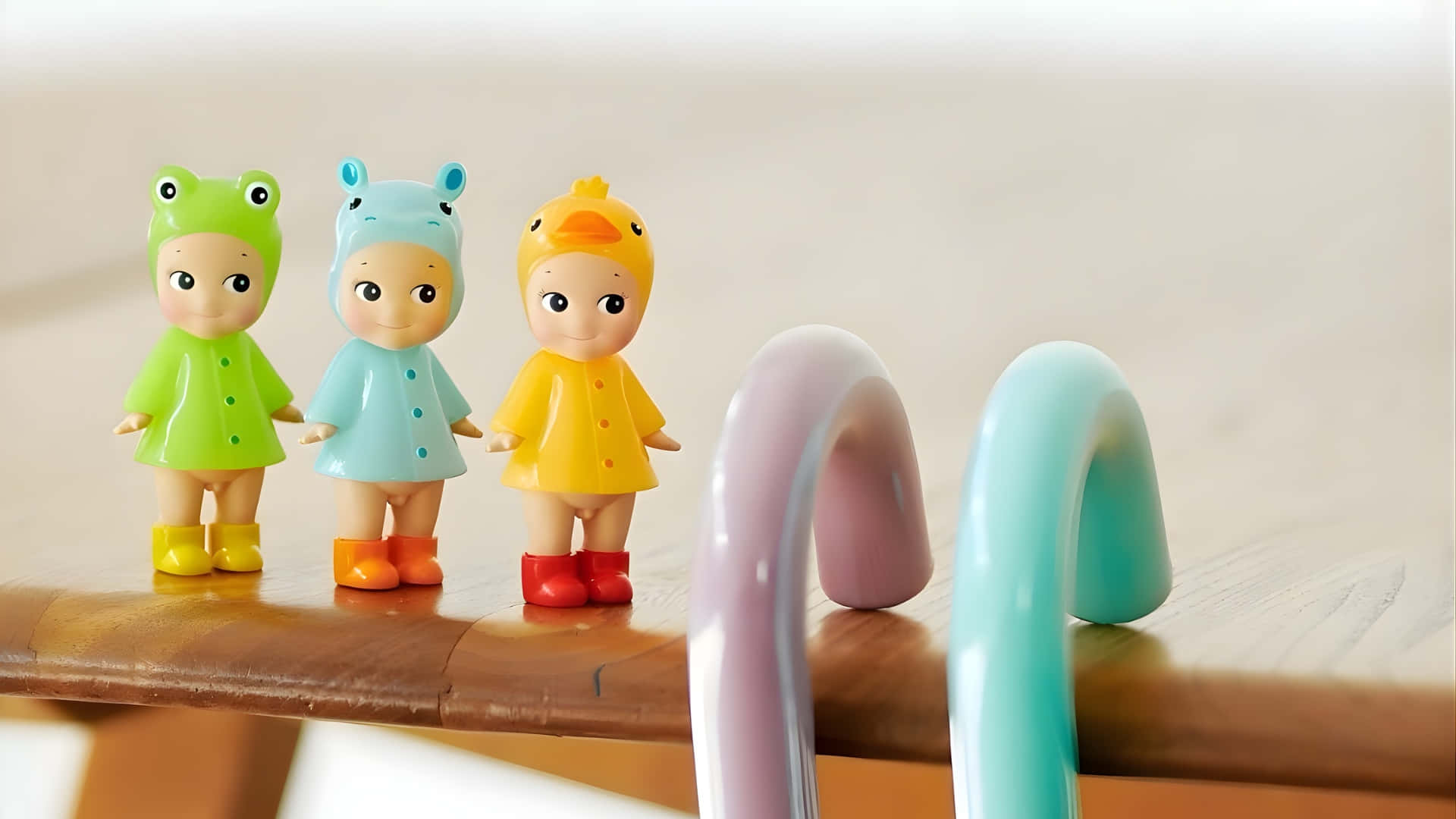  壁紙 — 三個色彩繽紛的Sonny公仔，穿著青蛙、河馬和鴨子雨衣，站在木質表面上，旁邊有粉彩彎曲物體。