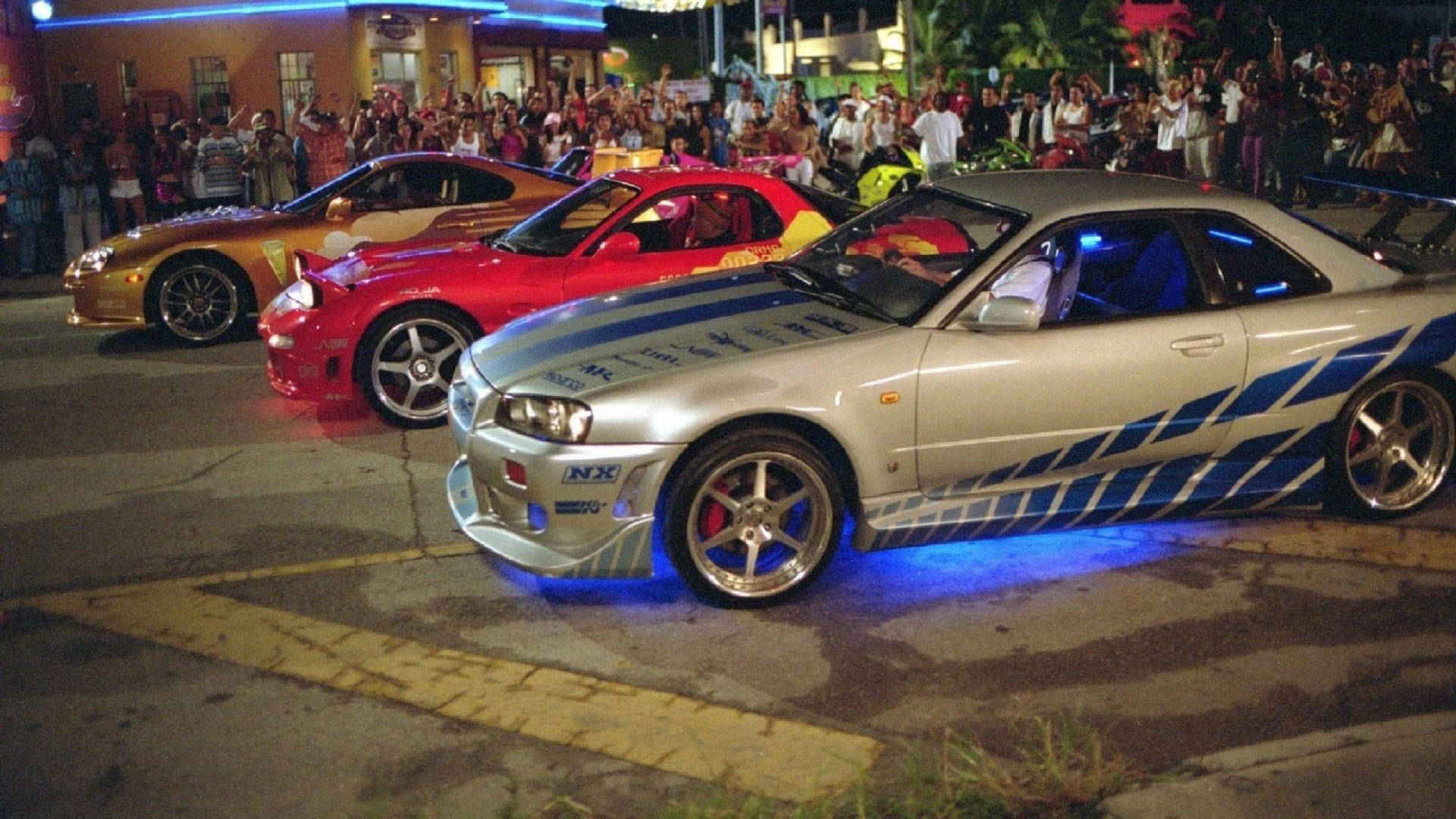 三輛定制街頭賽車在夜間停泊，帶有藍色車底燈光，人群觀看。 — 保羅·沃克汽車 壁紙