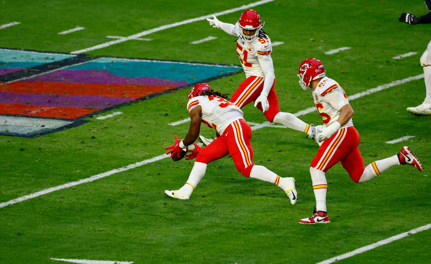  壁紙 — 三名身穿紅白球衣的足球運動員在體育場燈光下的翠綠球場上慶祝。