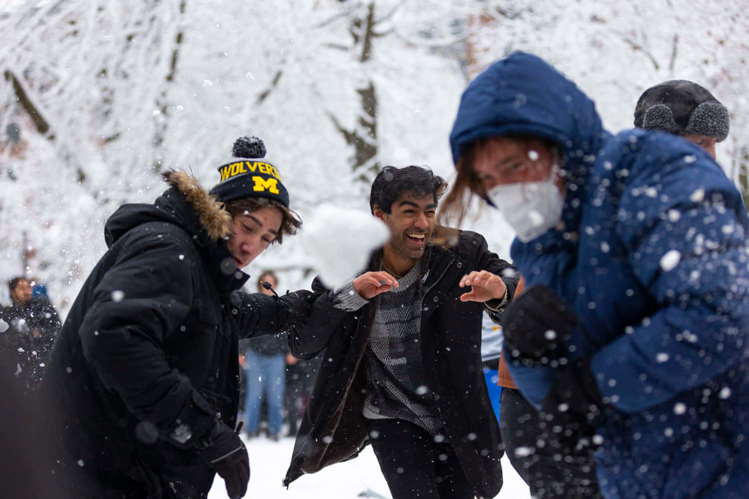  壁紙 — 三個朋友在雪景公園中大笑並嬉戲地互相推擠，雪花在他們周圍飄落。