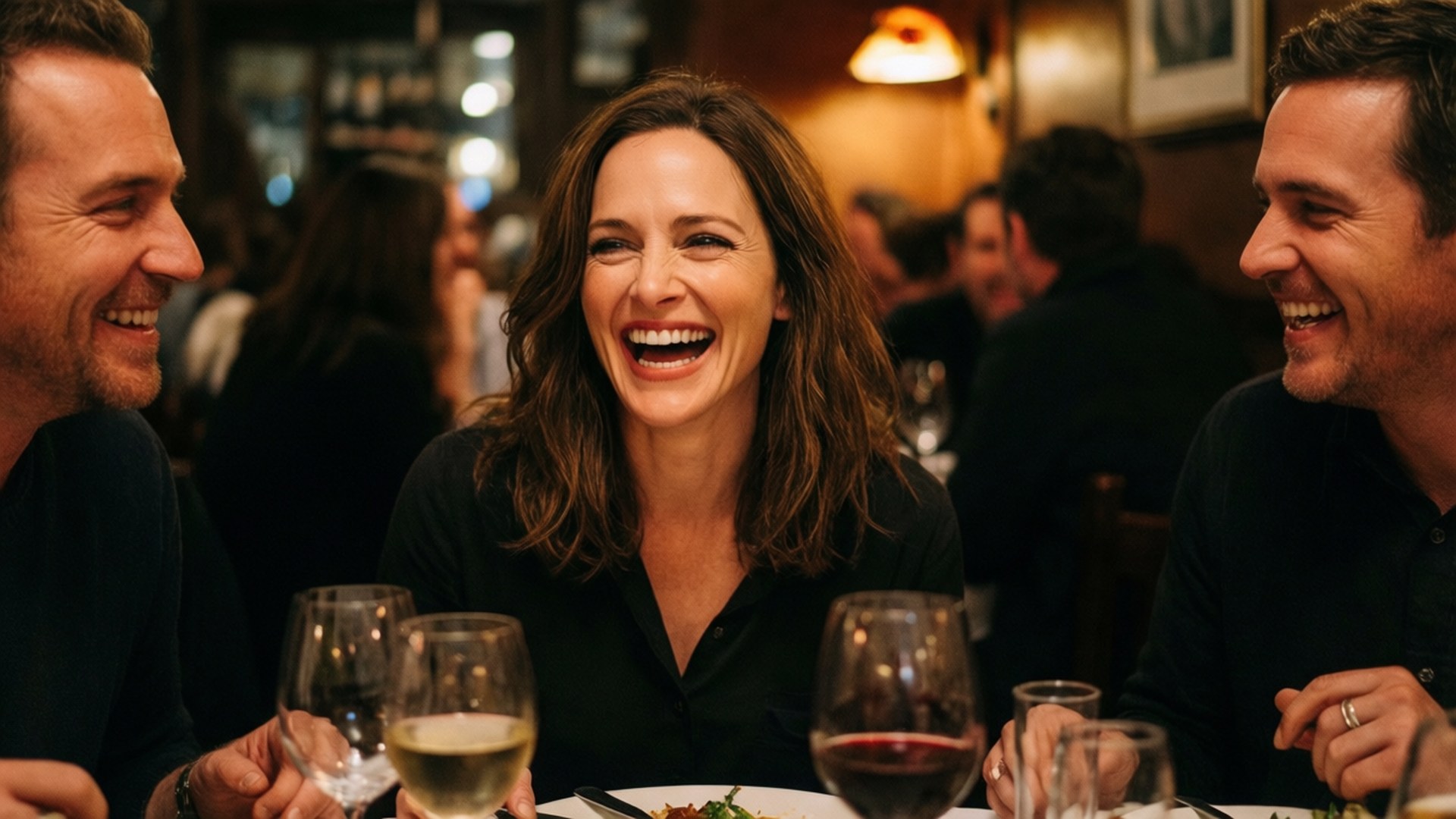 Rachel Mcadams 桌布 壁紙 — 三位朋友在燈光溫暖的餐廳桌上，一邊喝酒一邊開懷大笑。