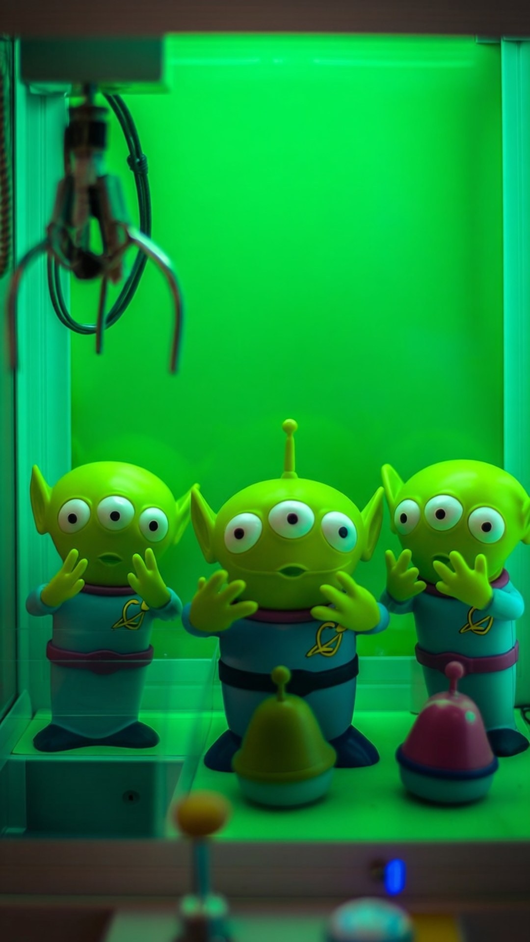 Alien Worship Claw 壁紙 — 三個綠色三眼外星人玩具在夾娃娃機中，沐浴在霓虹綠光下。