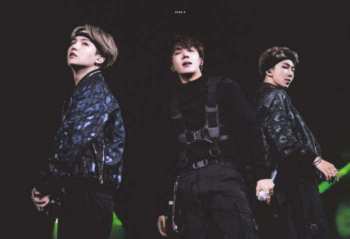 三位男性表演者在綠色燈光下的舞台上穿著深色服裝。 — Bts 壁紙