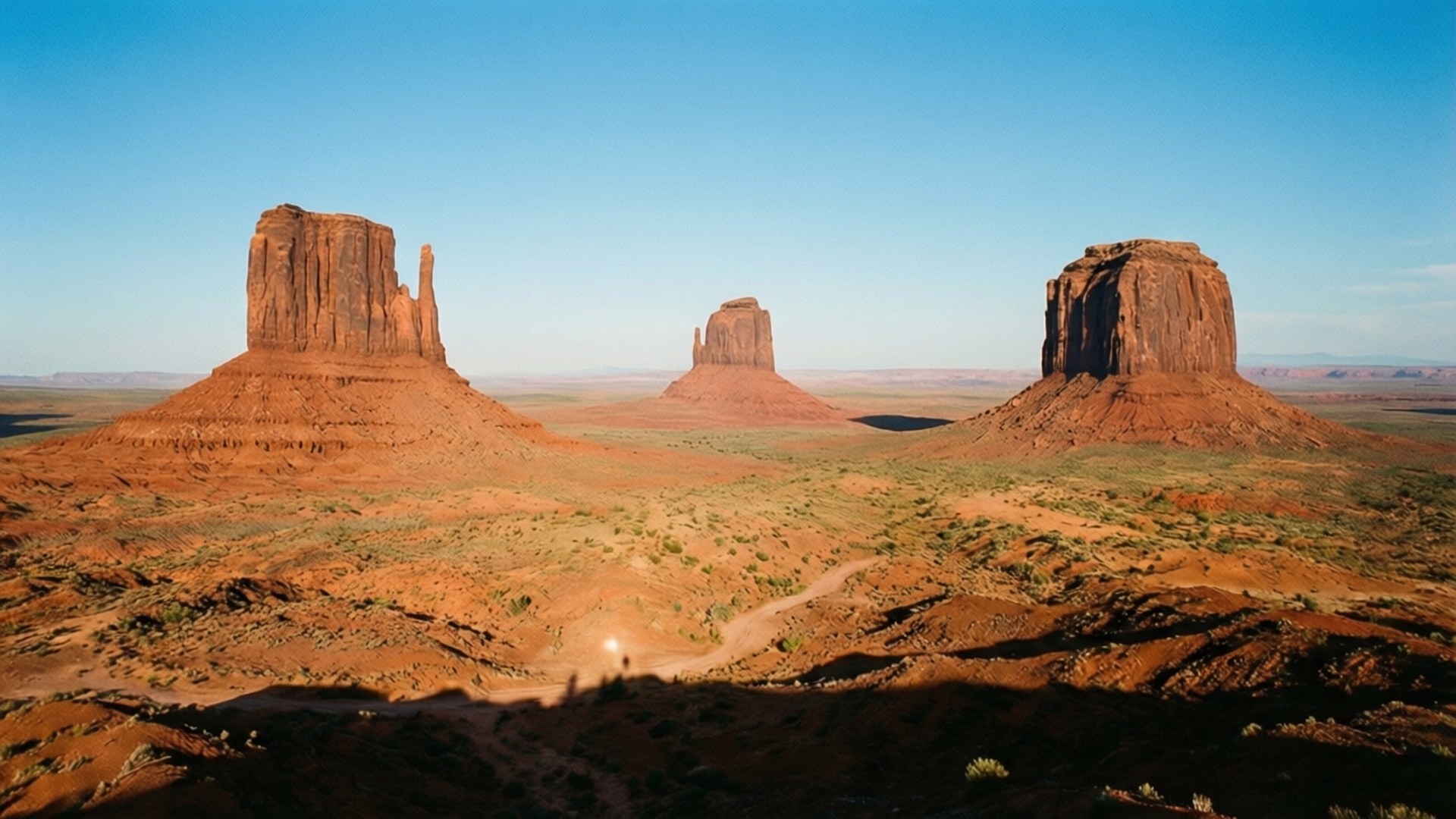 Monument Valley Vistas 壁紙 — 三座巨大的紅色砂岩但丁從廣闊的沙漠平原升起，在清澈的藍天下。