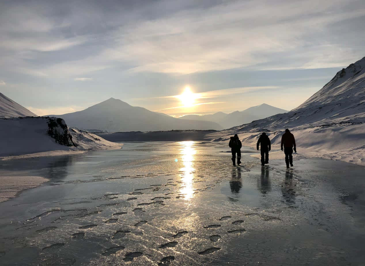  壁紙 — 三個剪影人物在日出時走過結冰的湖面，背景是白雪覆蓋的山脈。