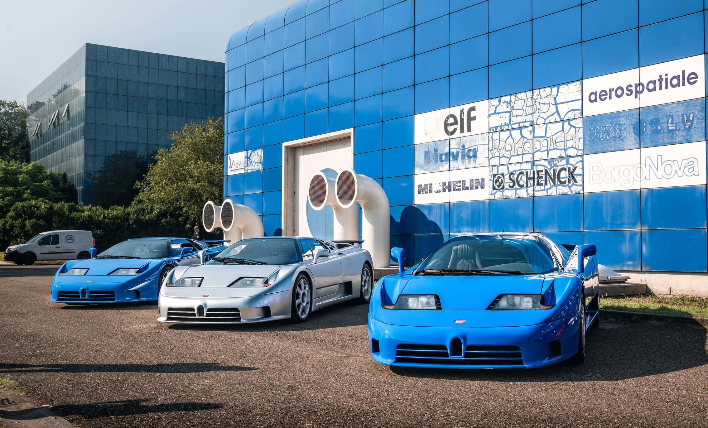 Bugatti Eb110 桌布 壁紙 — 三輛時尚的藍銀色Bugatti EB110超級跑車停在一棟帶有贊助商標誌的充滿活力的藍色玻璃建築前。