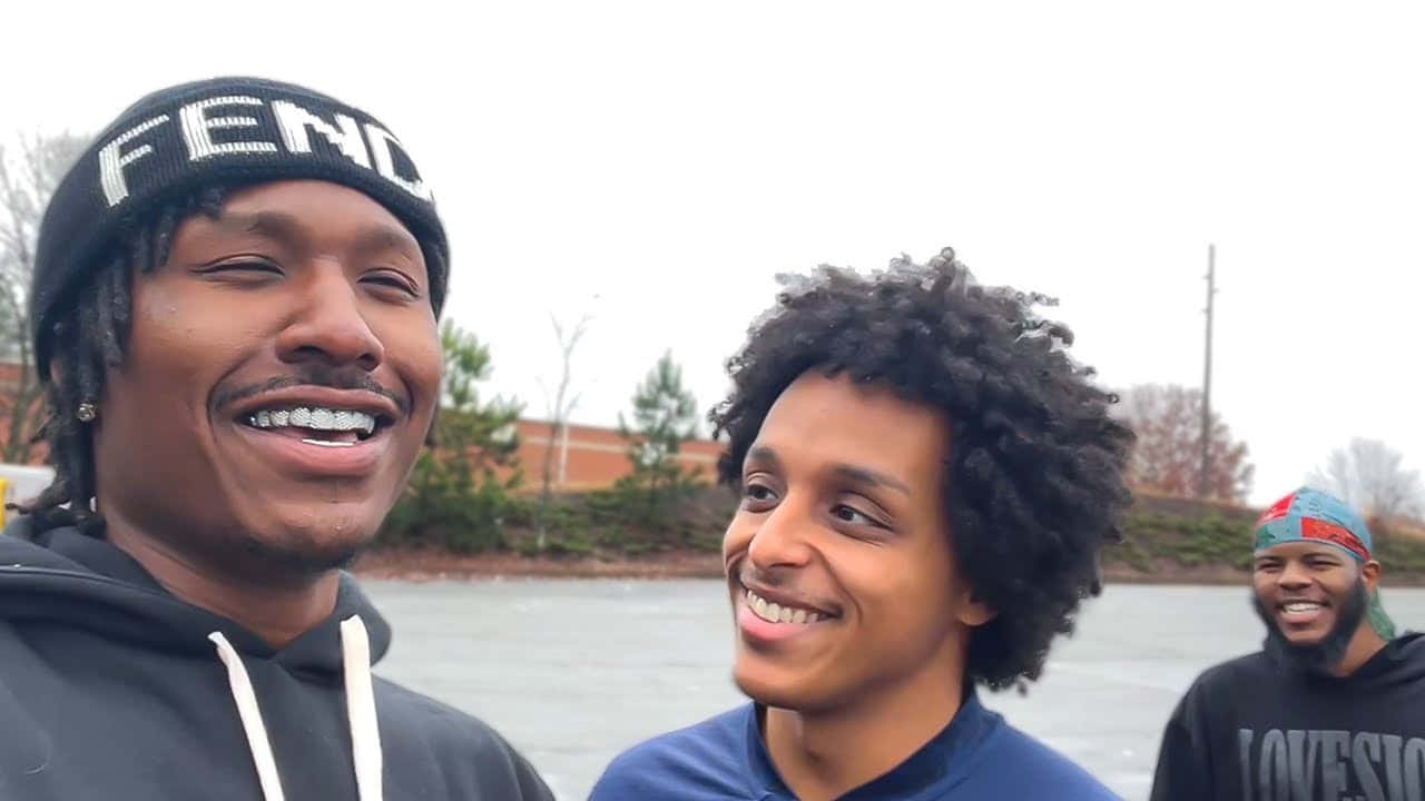 Duke Dennis 桌布 壁紙 — 三位微笑的年輕男子穿著休閒街頭服飾，在陰天時於戶外結冰的池塘附近一起大笑。
