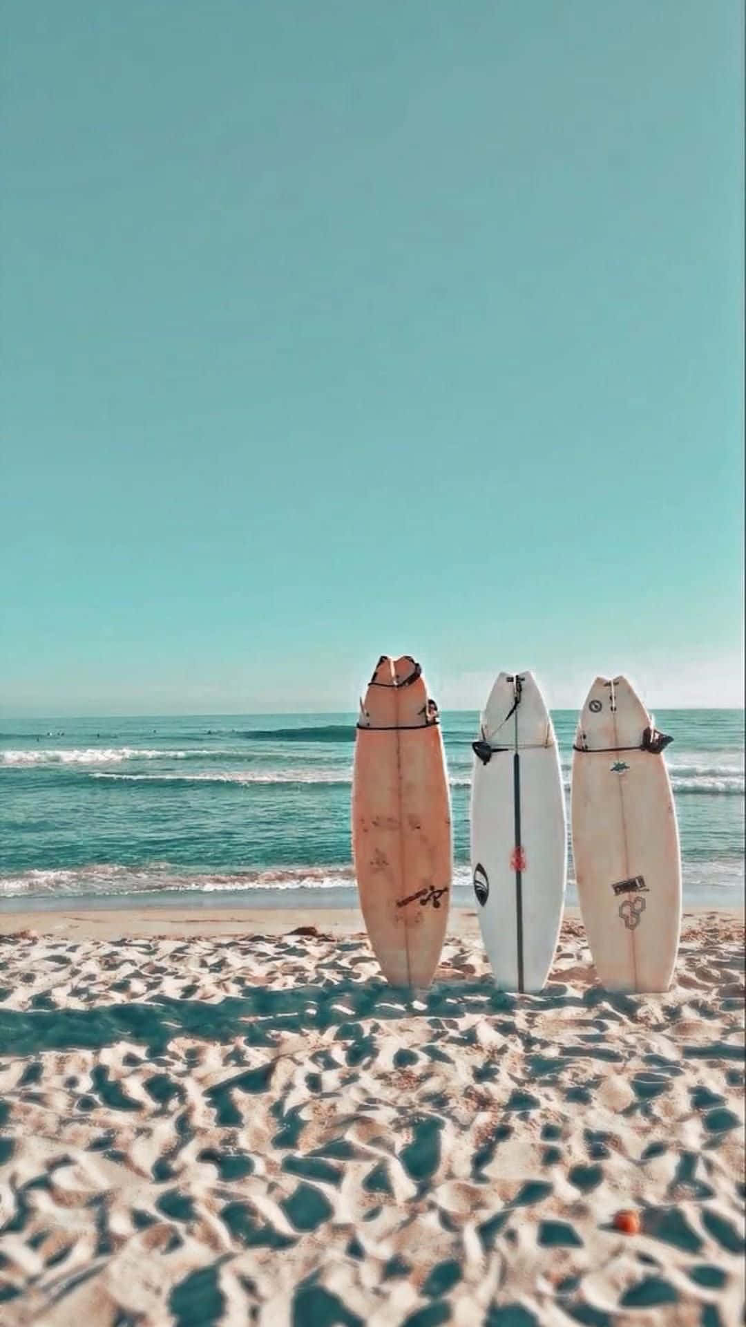  壁紙 — 三塊衝浪板直立於有紋理的沙地上，面向碧綠海洋，天空晴朗。