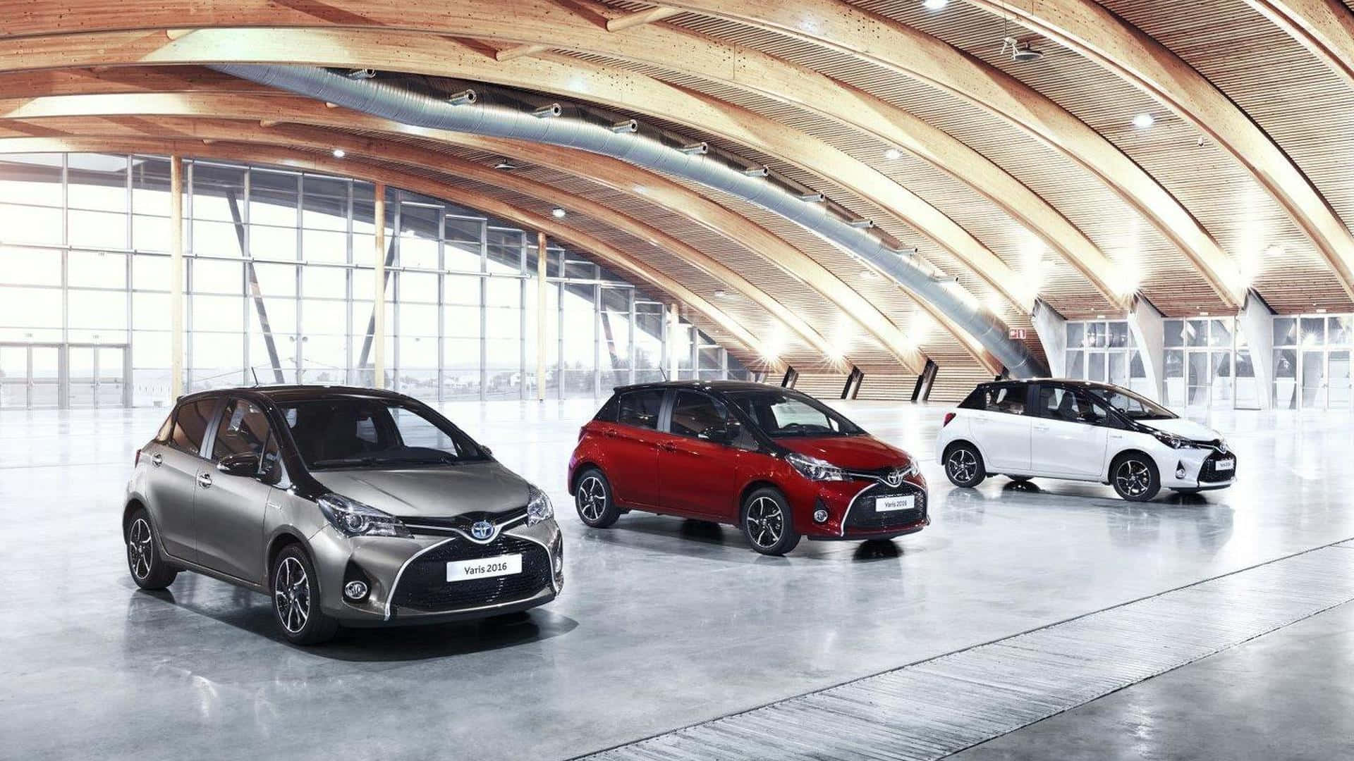 三輛豐田Yaris 2016汽車，銀色、紅色和白色，在現代建築展廳中展示。 — Toyota Supra 壁紙