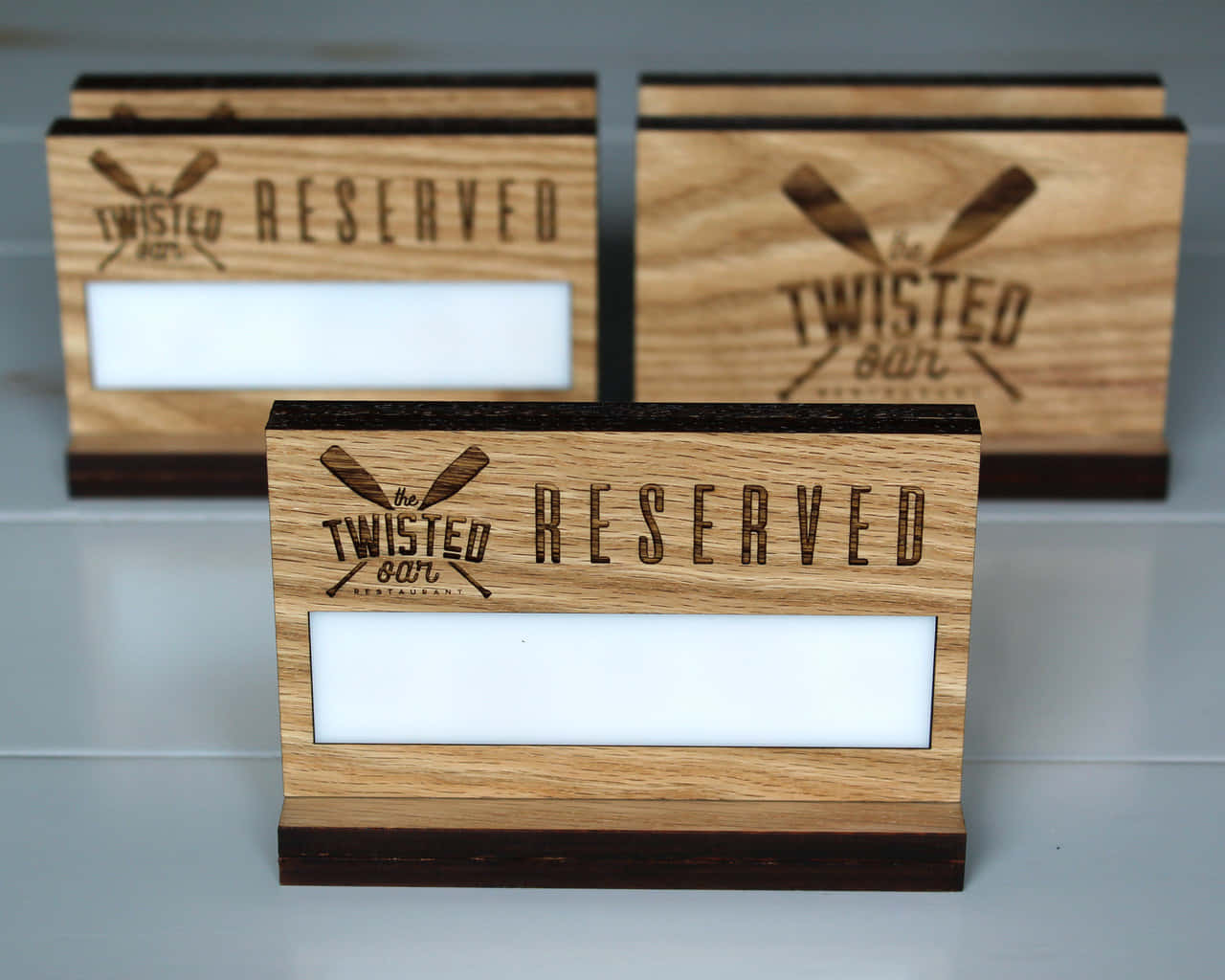 Reserved 桌布 壁紙 — Twisted Bar Restaurant 的三個木製預訂牌，帶有交叉蝙蝠標誌和空白名牌，放在灰色檯面上。