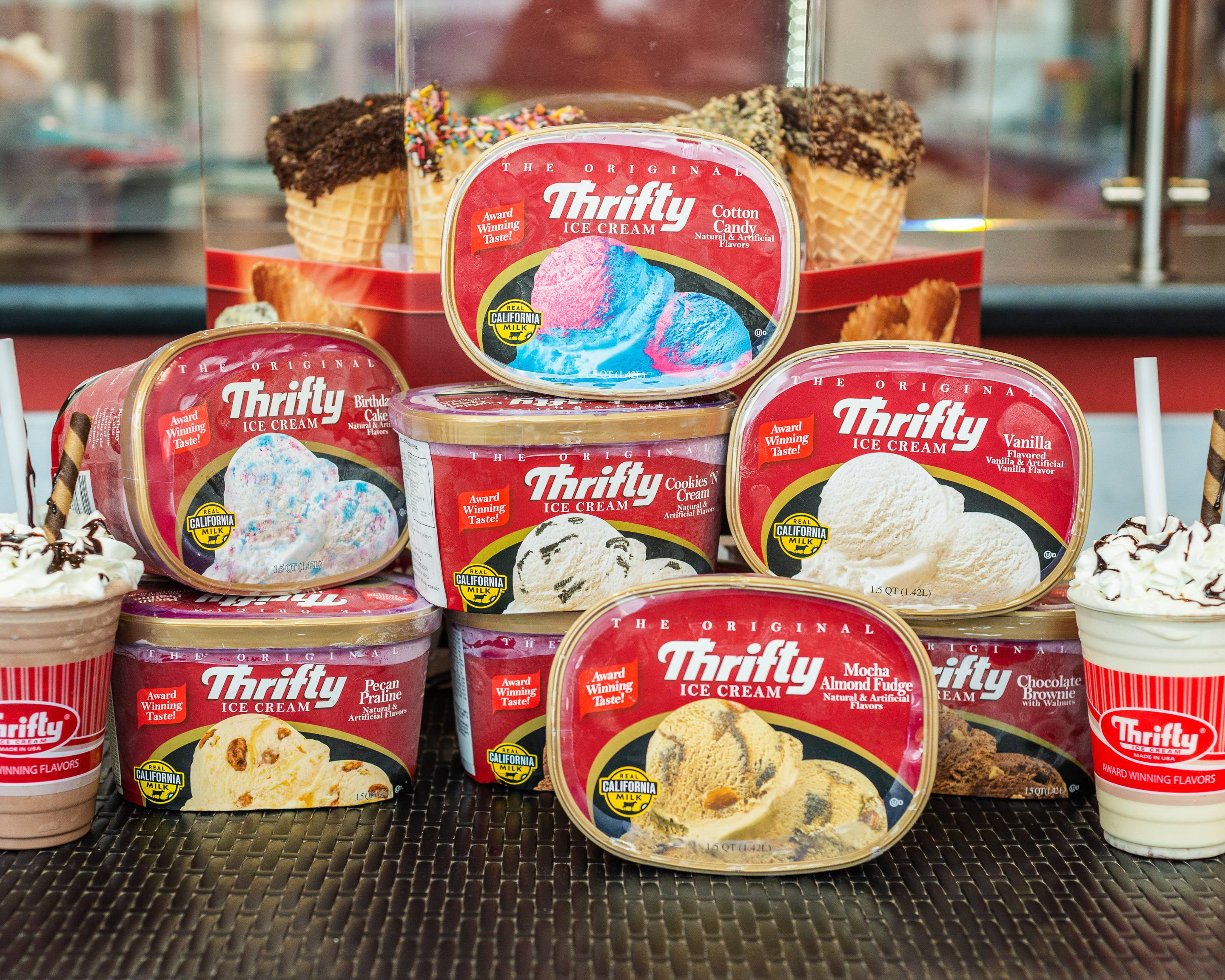 Ice Cream 桌布 壁紙 — Thrifty Ice Cream 桶裝冰淇淋和聖代在深色紋理櫃檯上色彩繽紛的陳列，搭配多種口味的冰淇淋球和配料。