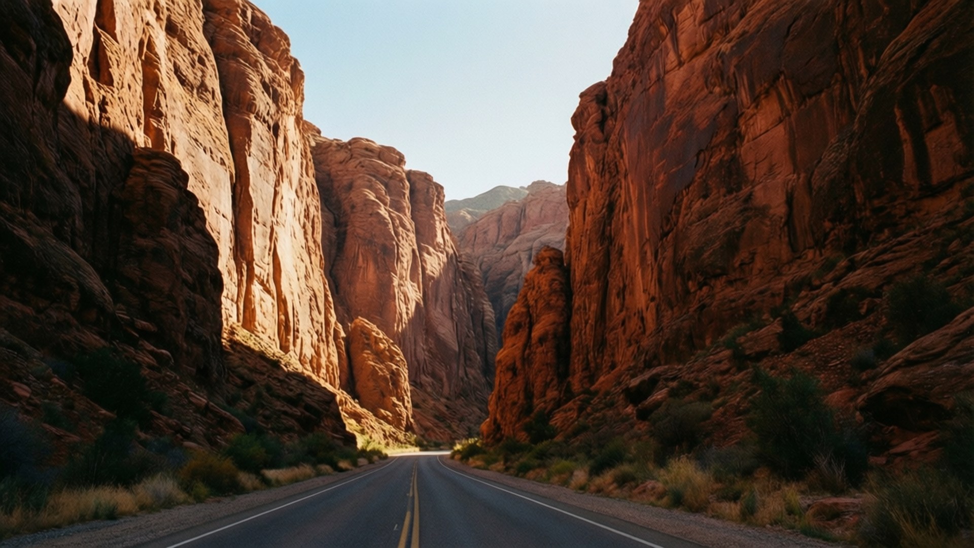 Canyon Road 壁紙 — 一條筆直的柏油路蜿蜒穿過高聳的紅色岩壁，在清澈的藍天下。