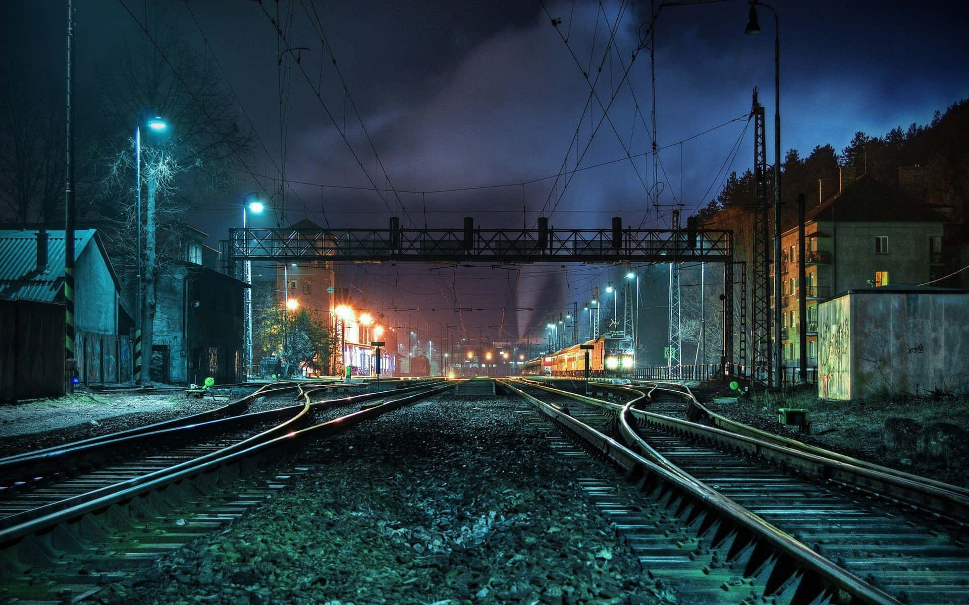  壁紙 — 鐵路軌道在陰沉的夜空下匯合，一列火車亮著車頭燈駛近。