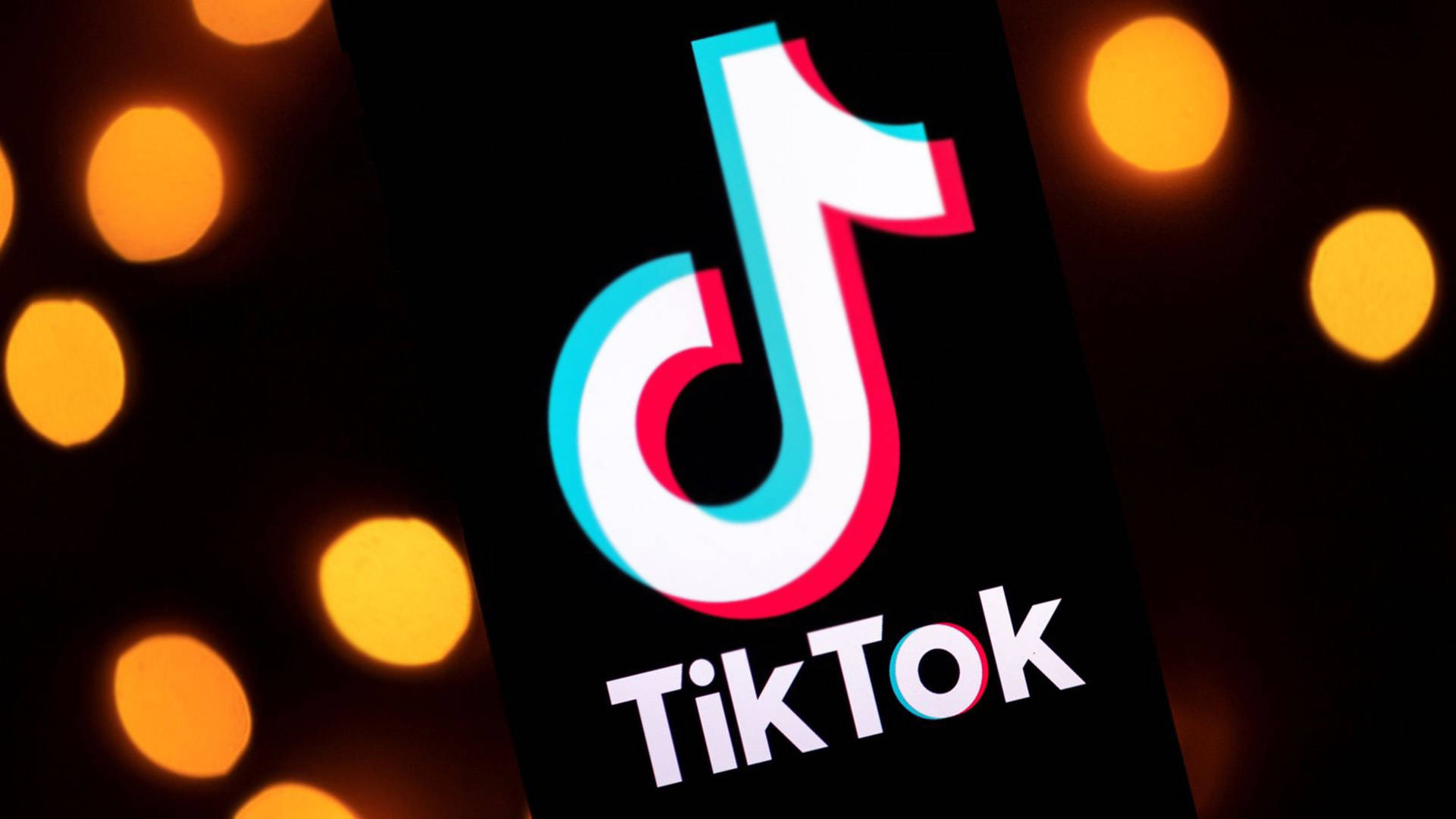 TikTok 動圖 桌布 壁紙 — TikTok 標誌在手機螢幕上發光，背景是溫暖的橙色散景燈光。