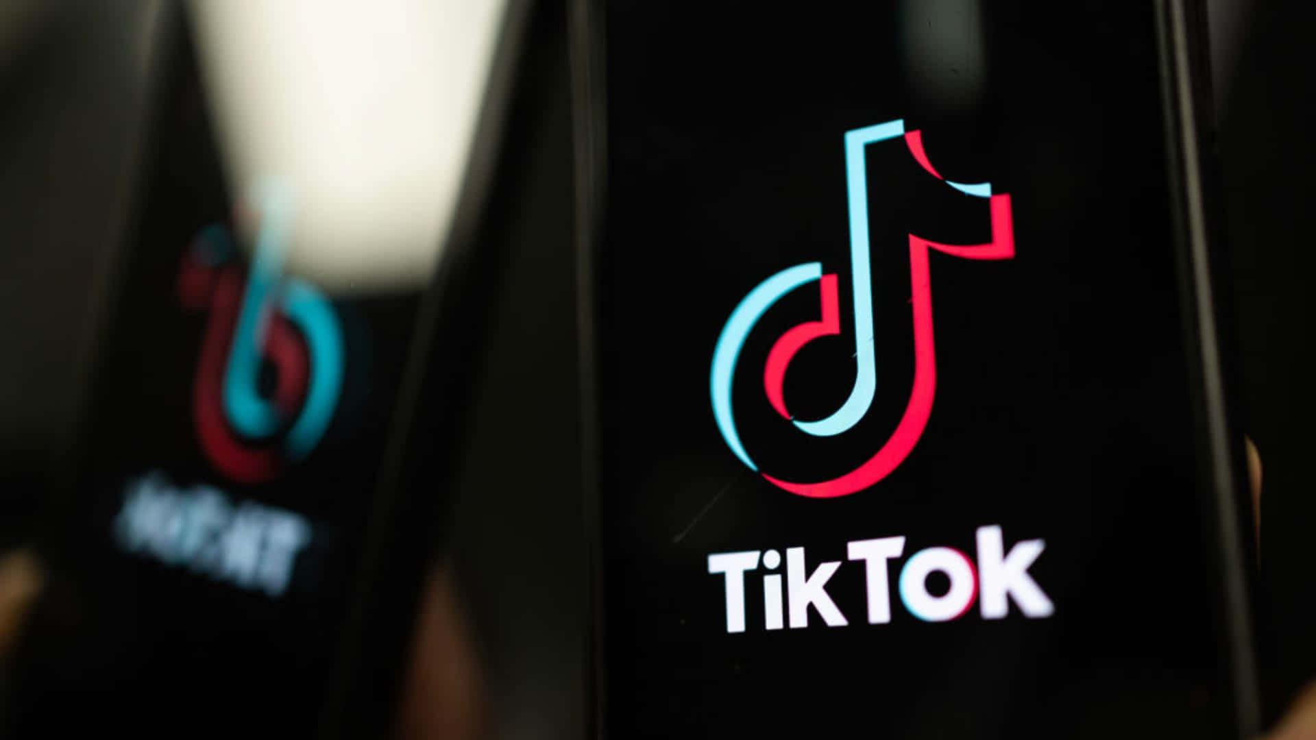 TikTok 動圖 桌布 壁紙 — TikTok應用程式標誌在昏暗環境中於智慧型手機螢幕上發光的特寫。