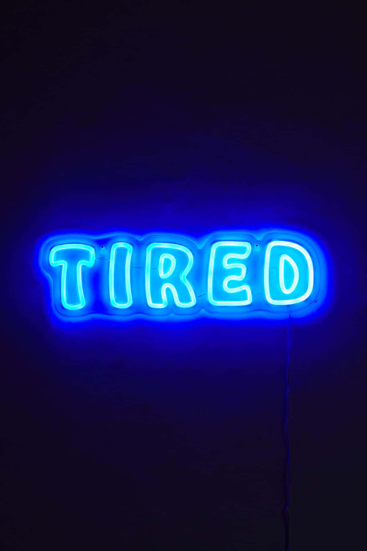  壁紙 — 一個發光的藍色霓虹燈牌，拼寫出TIRED，在昏暗的房間中對著深色牆壁散發出柔和的光芒。