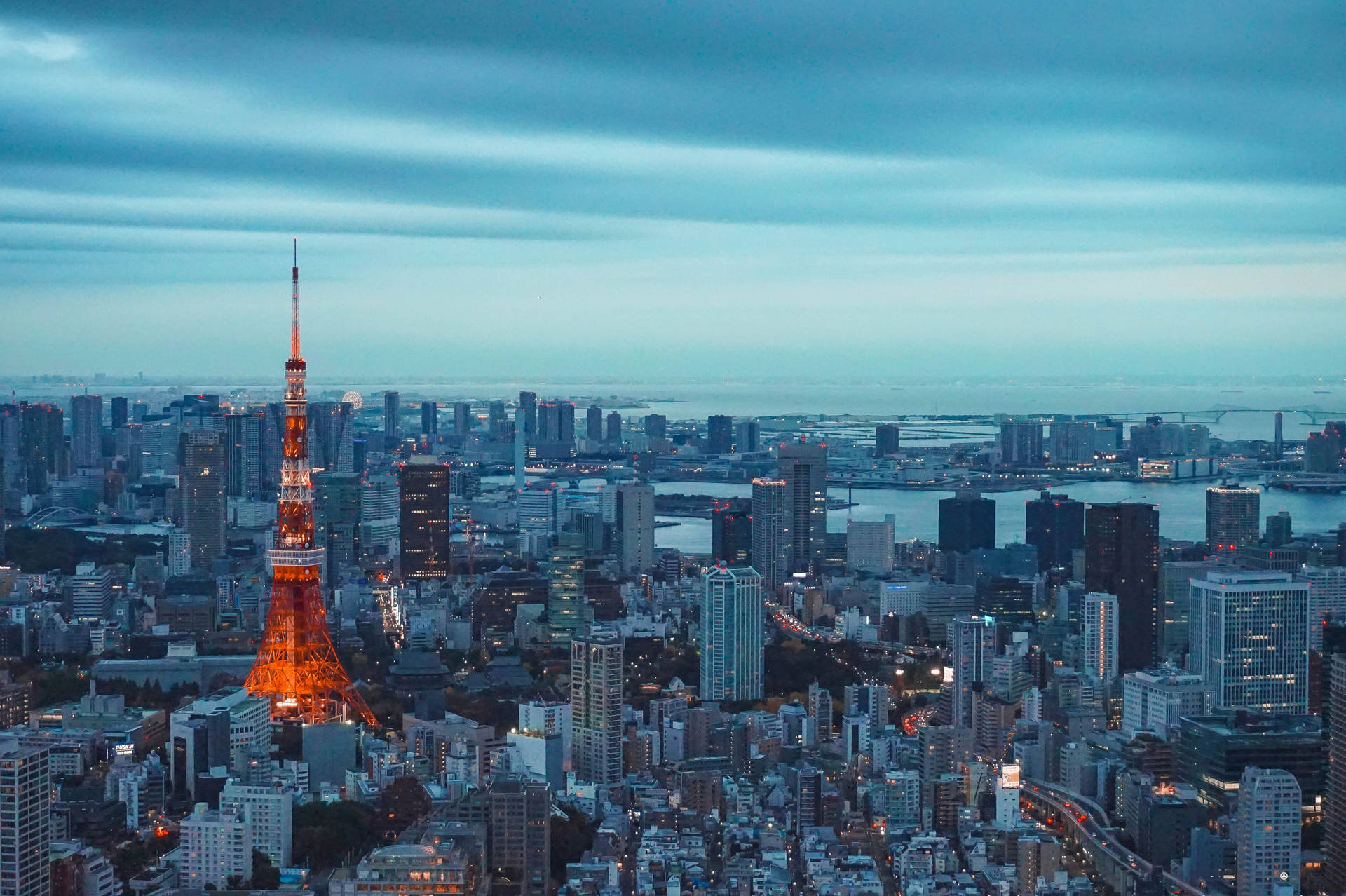 黃昏時分點亮的東京塔，背景有城市燈光和水面 — 東京鐵塔 壁紙