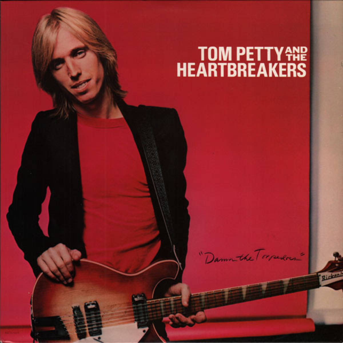 rock n roll 桌布 壁紙 — Tom Petty 在鮮紅色背景前手持吉他，白色文字標明他及其樂團的身份。