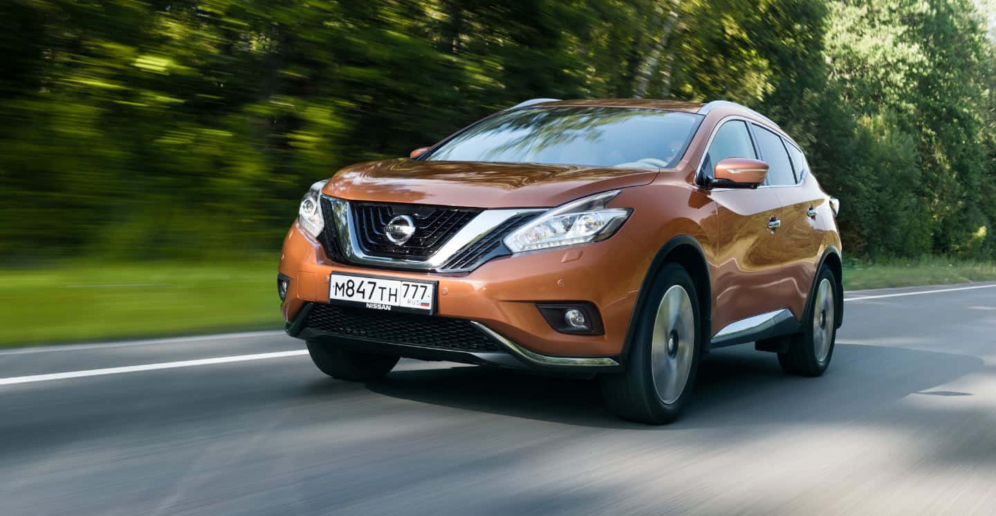 Nissan Murano 桌布 壁紙 — 一輛銅色的日產Rogue SUV在陽光明媚的道路上疾馳，茂密的綠樹因運動而模糊。
