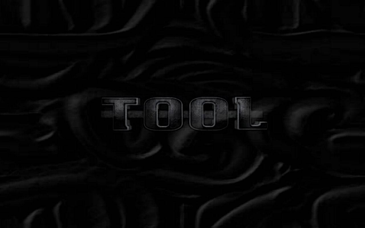 工具 桌布 壁紙 — 「TOOL」一詞在黑暗、漣漪般的黑色布料背景上以金屬字母微弱發光。
