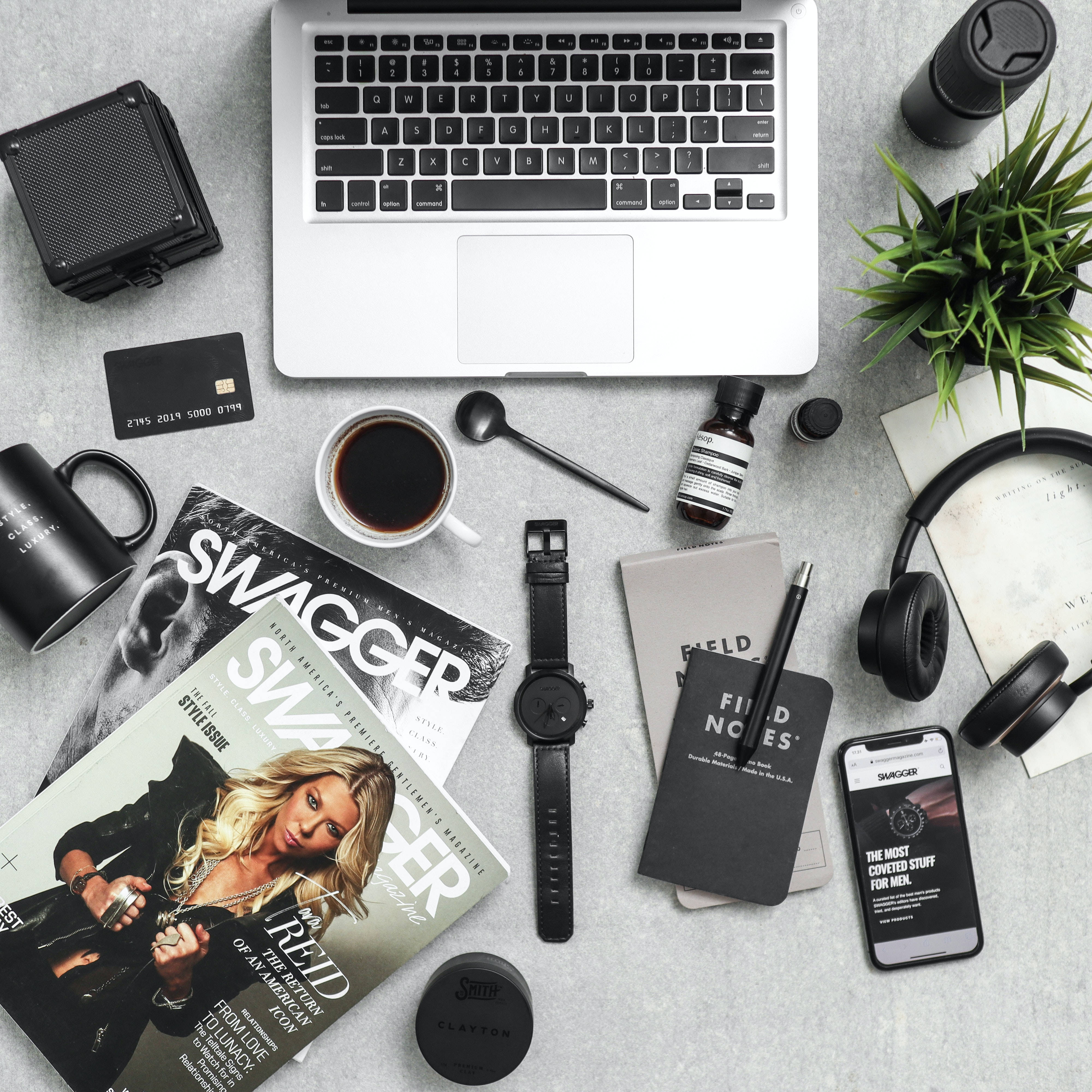 酷炫iPhone 桌布 壁紙 — Top-down view of a minimalist gray desk with a laptop coffee mug headphones and men's magazines arranged neatly.