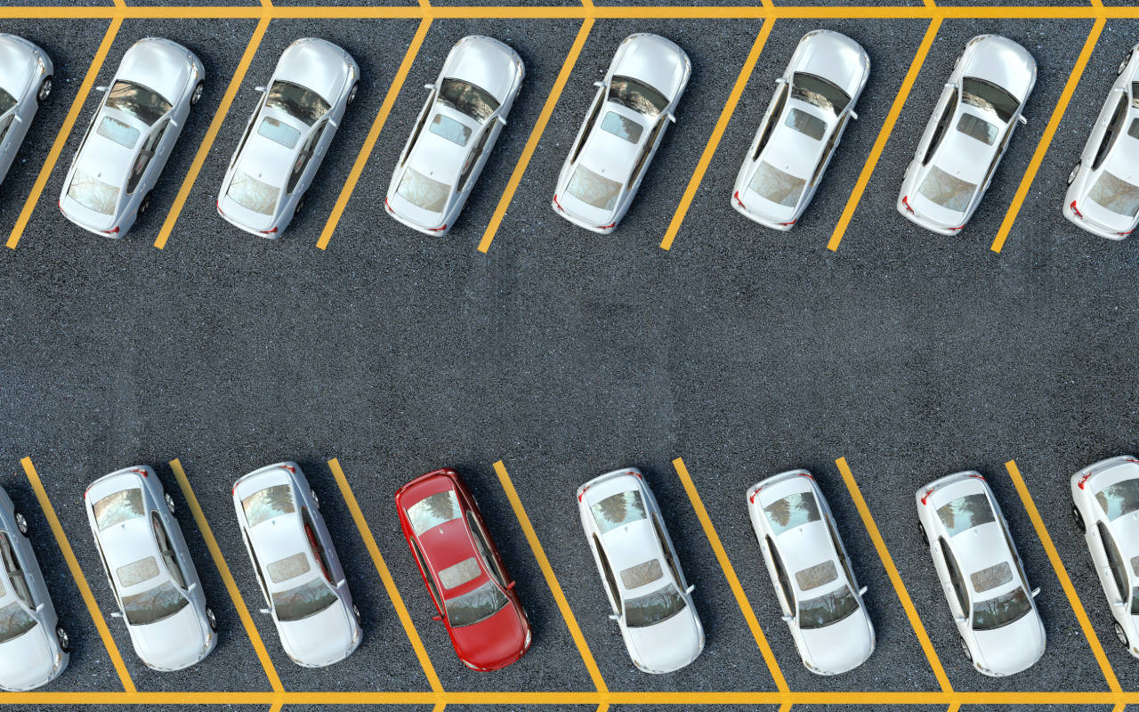 汽車 桌布 壁紙 — Top-down view of a parking lot with rows of silver cars and one striking red car parked among them.