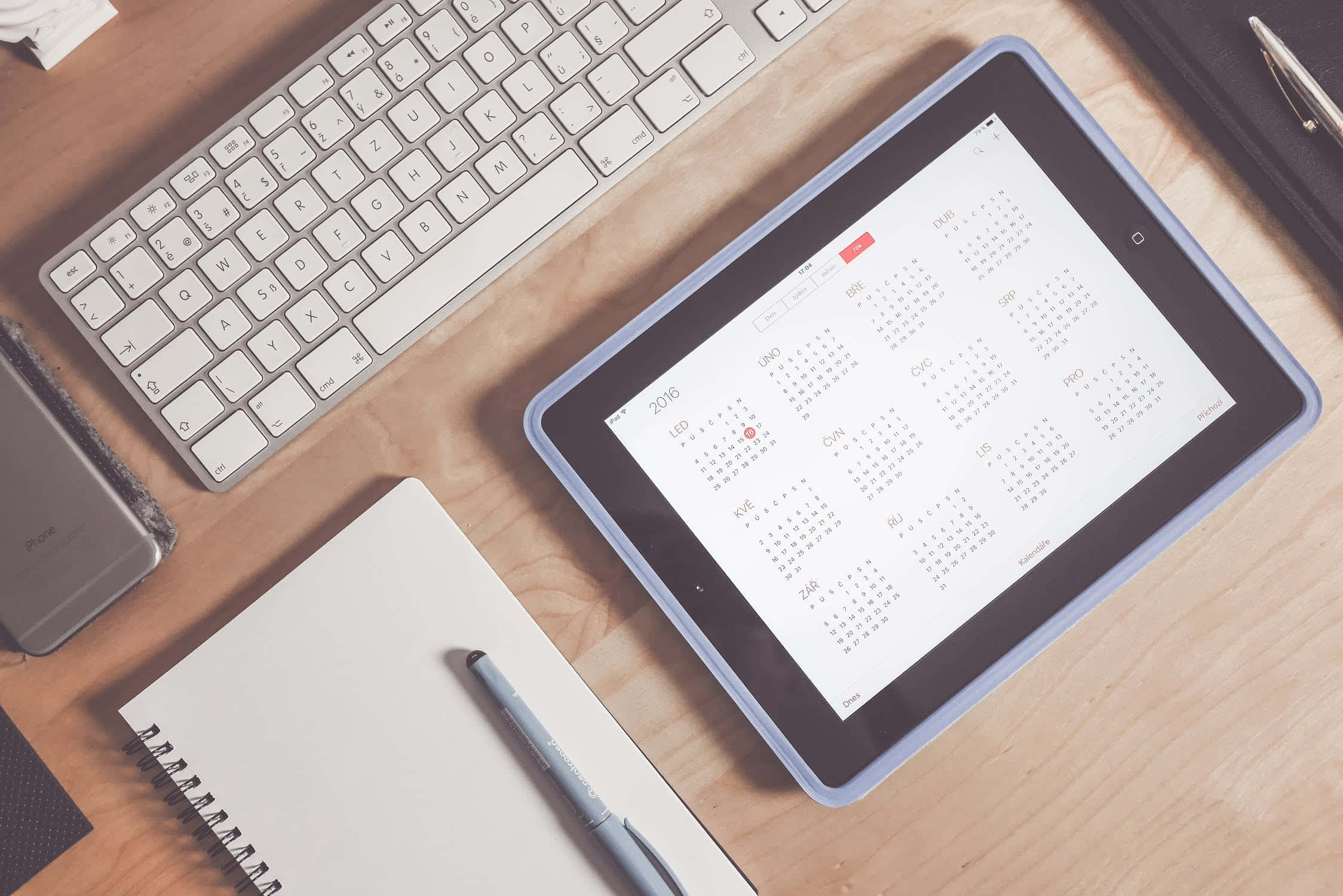 平板電腦 桌布 壁紙 — Top-down view of a wooden desk with a tablet displaying a calendar keyboard notebook and pen arranged for productivity.