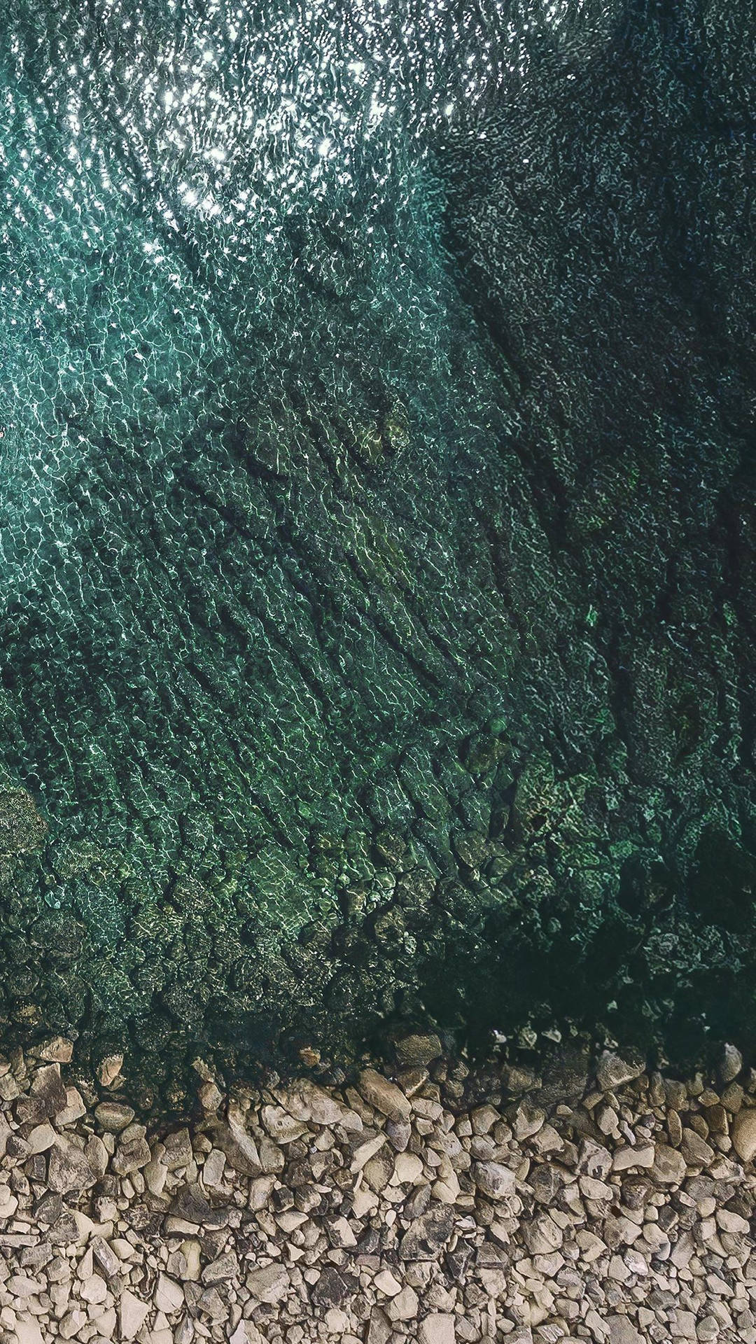 清澈碧綠的海水在岩石海岸上泛起漣漪，陽光閃爍。 — iPad 壁紙