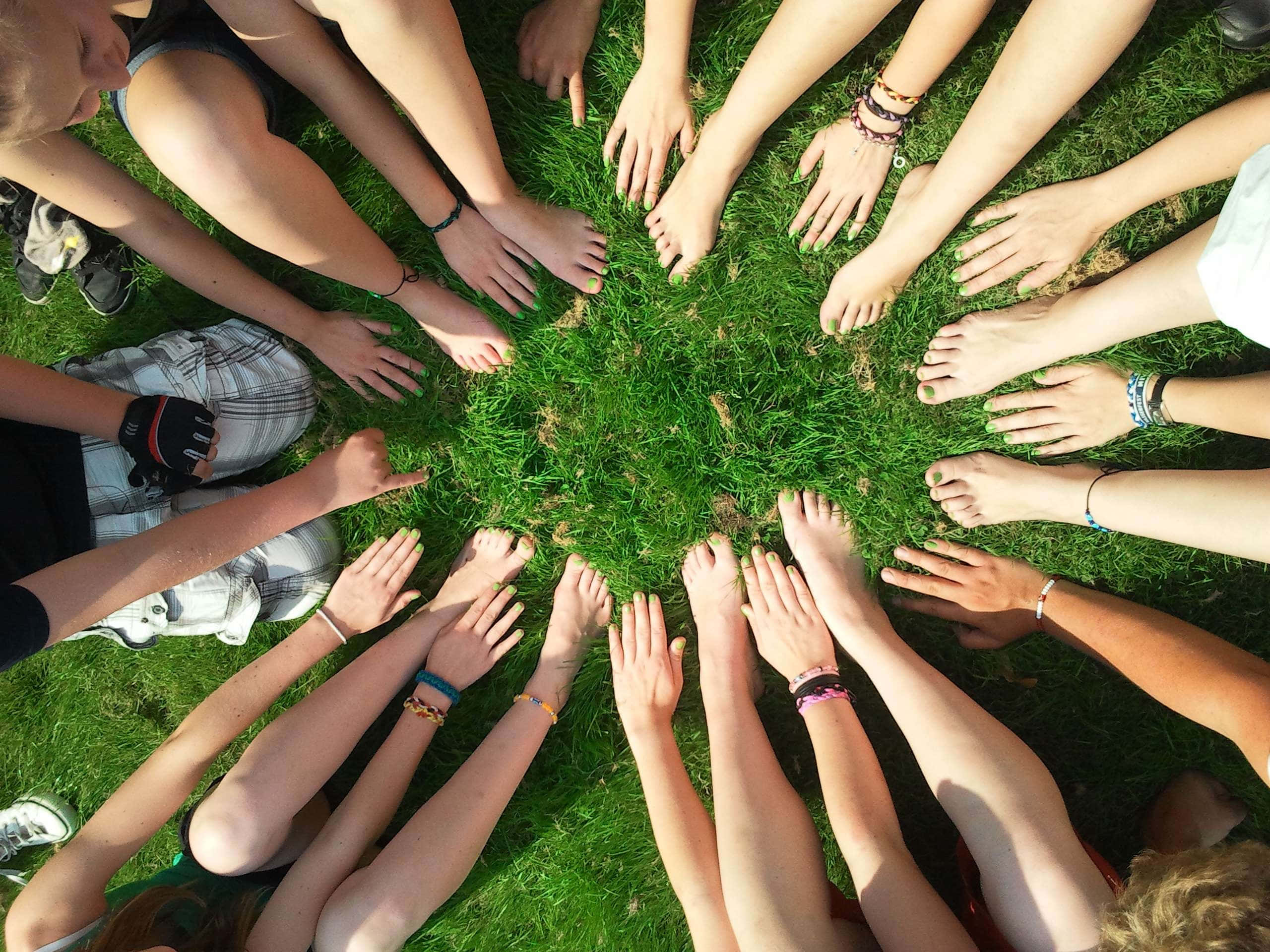 hands 桌布 壁紙 — Top-down view of diverse young people sitting barefoot in a circle on vibrant green grass with hands and feet touching.