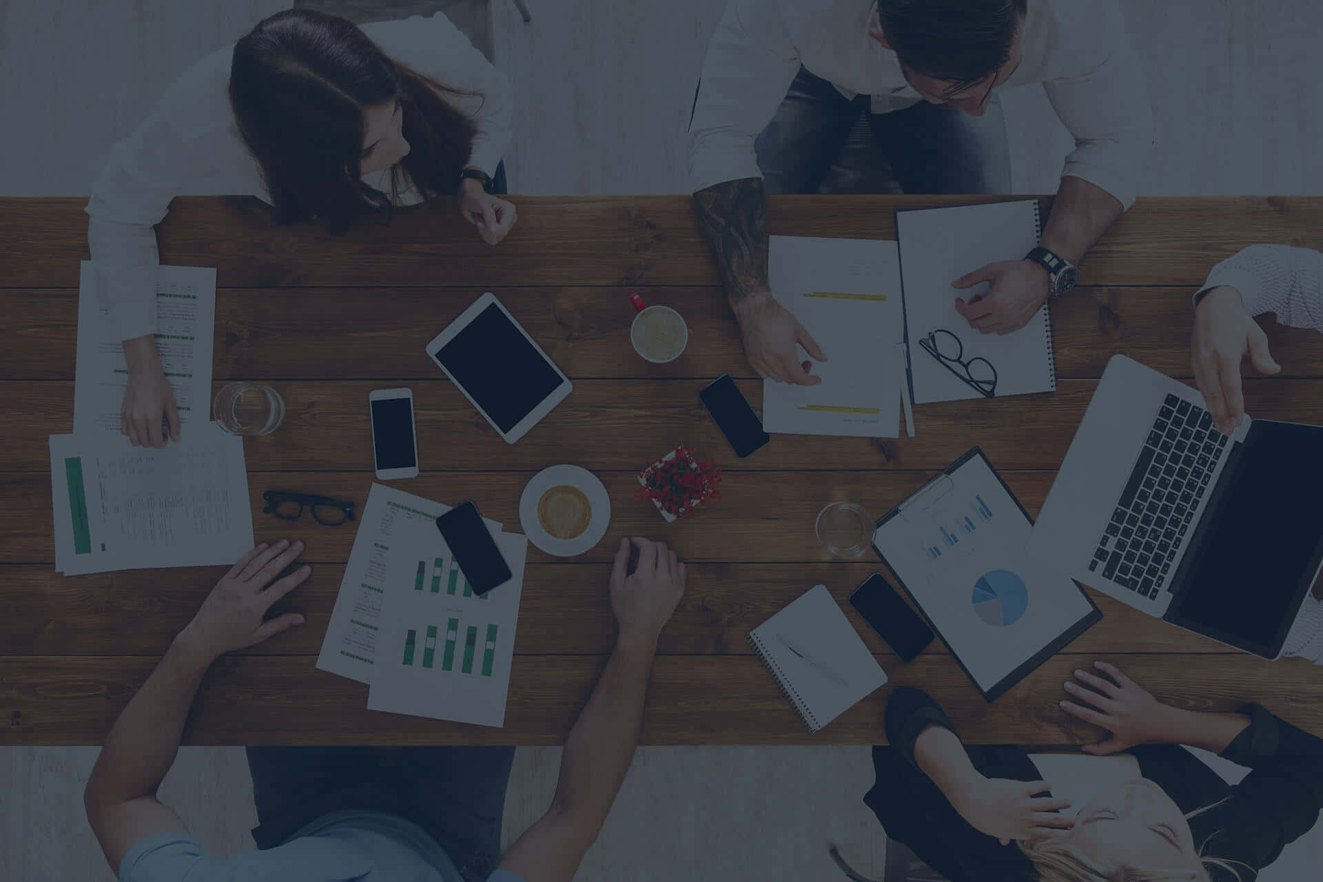 Work 桌布 壁紙 — Top-down view of four people collaborating around a wooden table filled with laptops papers and coffee cups.