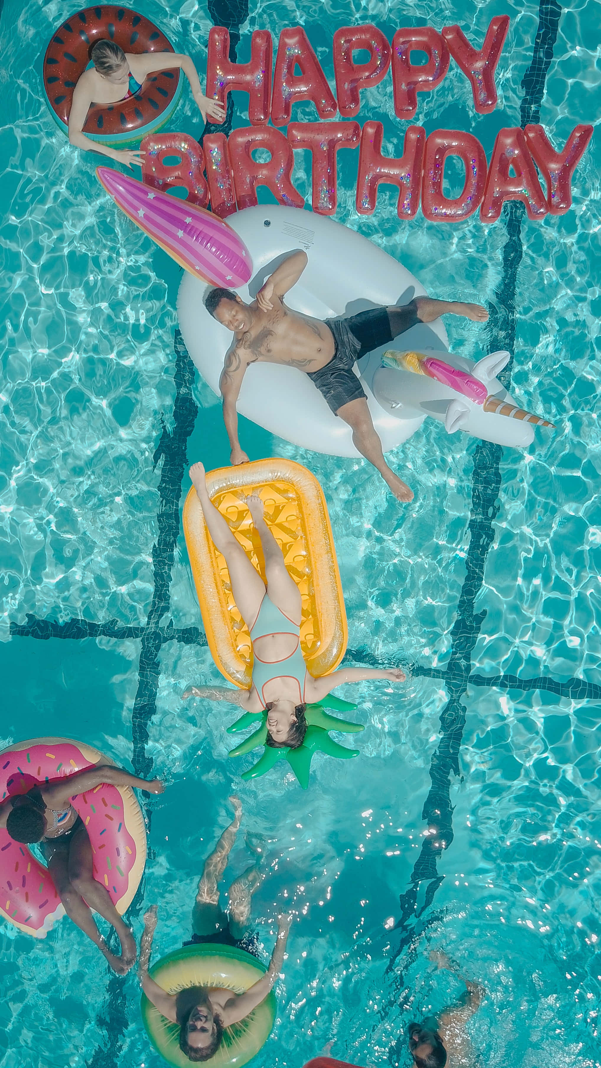 Cute Birthday 桌布 壁紙 — Top-down view of friends floating on colorful inflatable toys in a bright turquoise pool with a large HAPPY BIRTHDAY balloon.