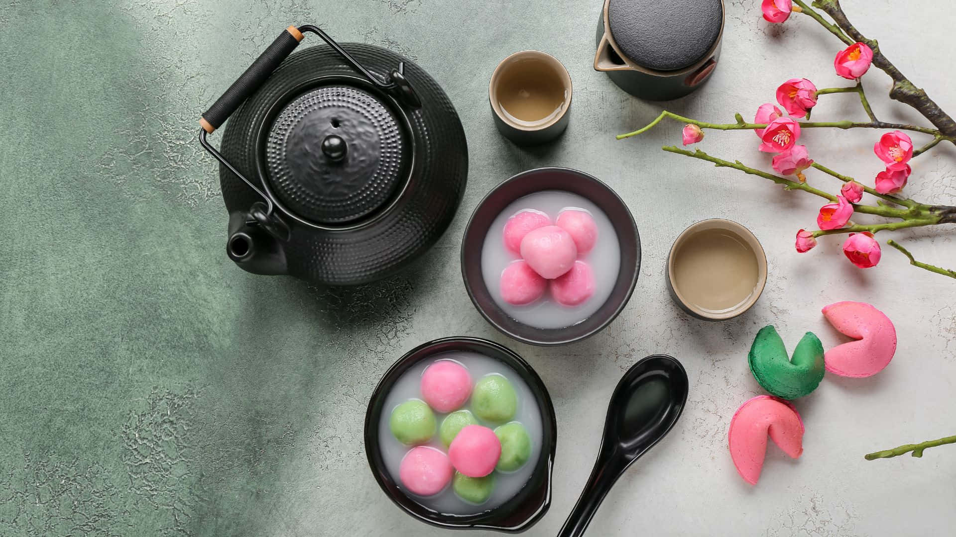  壁紙 — 傳統日本茶具套裝的俯視圖，碗中有粉紅色和綠色的麻糬糰子，旁邊有櫻花枝。