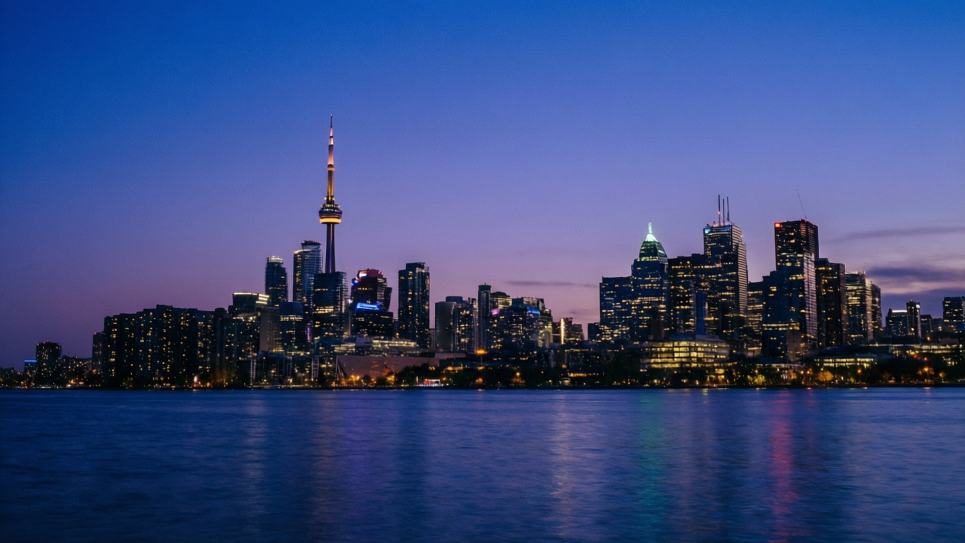 Toronto Blue Hour Panorama 壁紙 — 多倫多黃昏天際線，CN塔在深藍色天空下亮起，倒映在平靜的水面上。