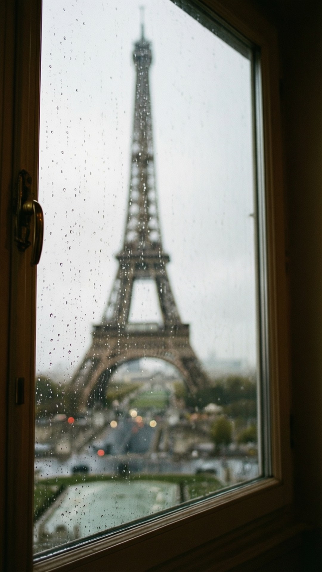 Rainy Window View 壁紙 — 透過佈滿雨點的窗戶看到的艾菲爾鐵塔，下方是模糊的城市燈光。