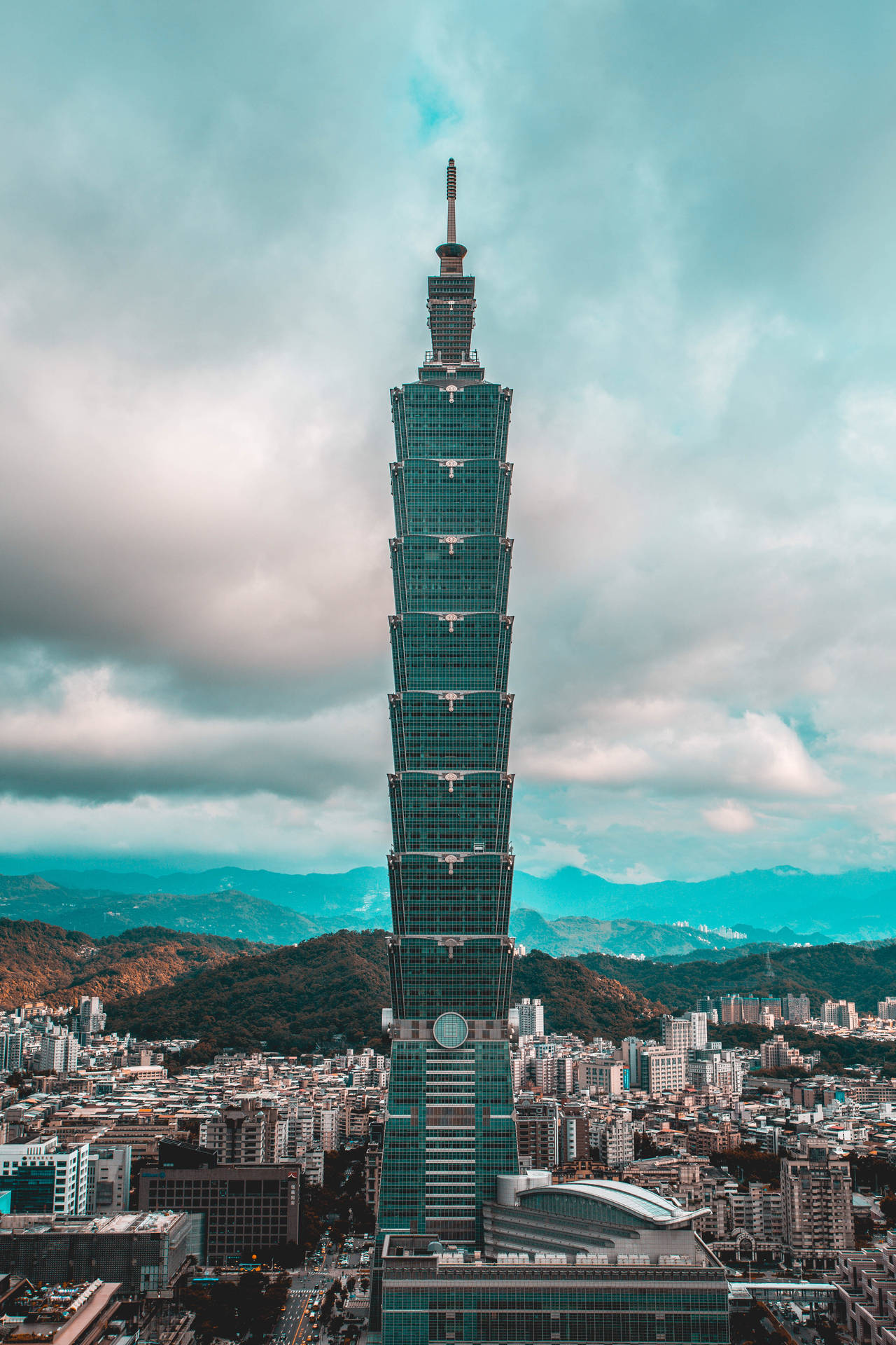 台北101摩天大樓聳立在密集的城市之上，背景有山脈。 — 台北 壁紙