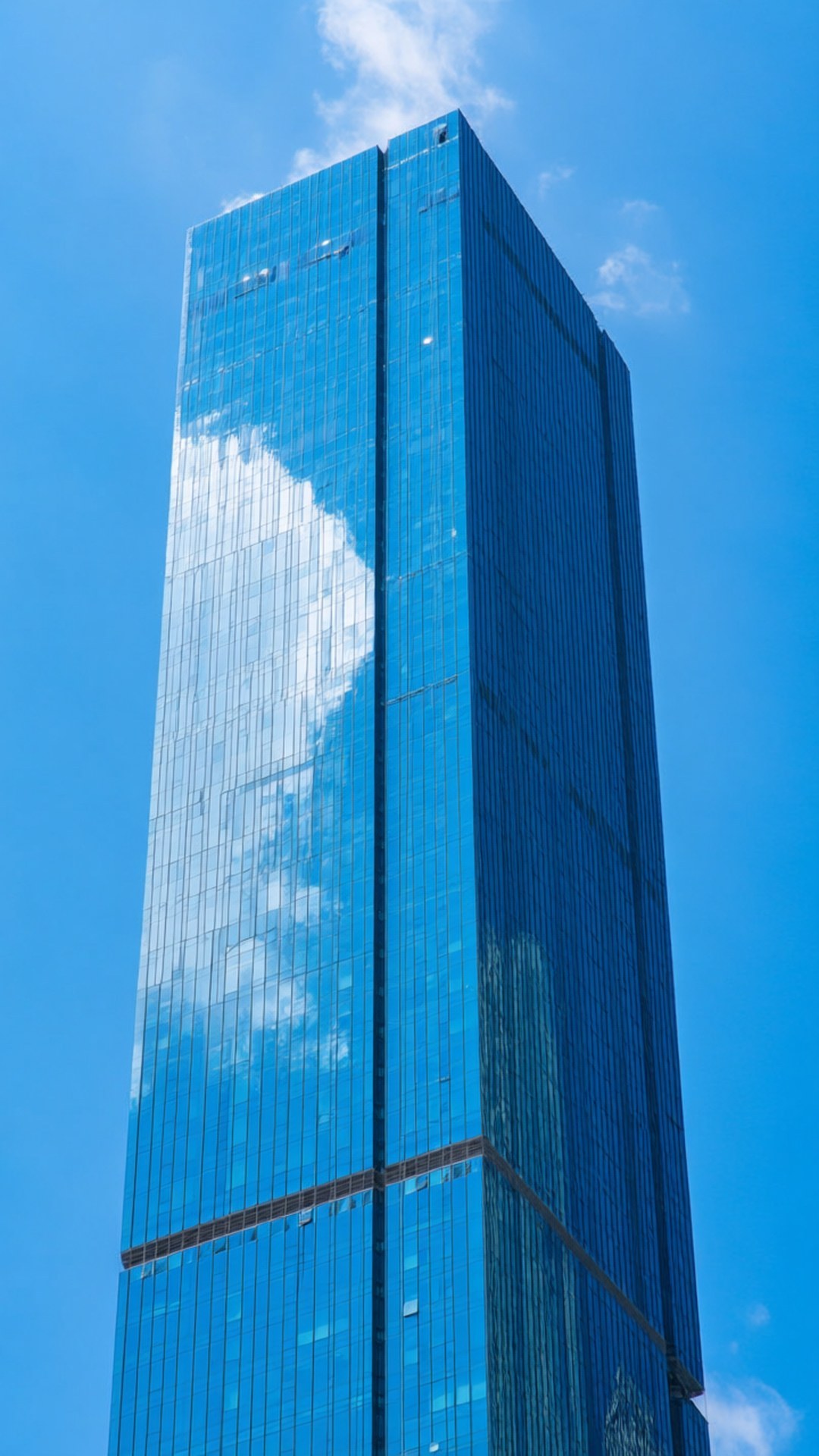 Sky Reflection Vertical 壁紙 — 一座高聳的玻璃摩天大樓在湛藍的天空下反射出蓬鬆的白雲。